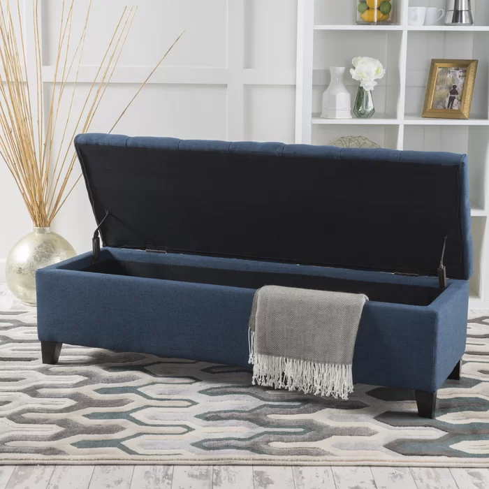 Tufted navy blue storage ottoman with open lid grey throw draped over side