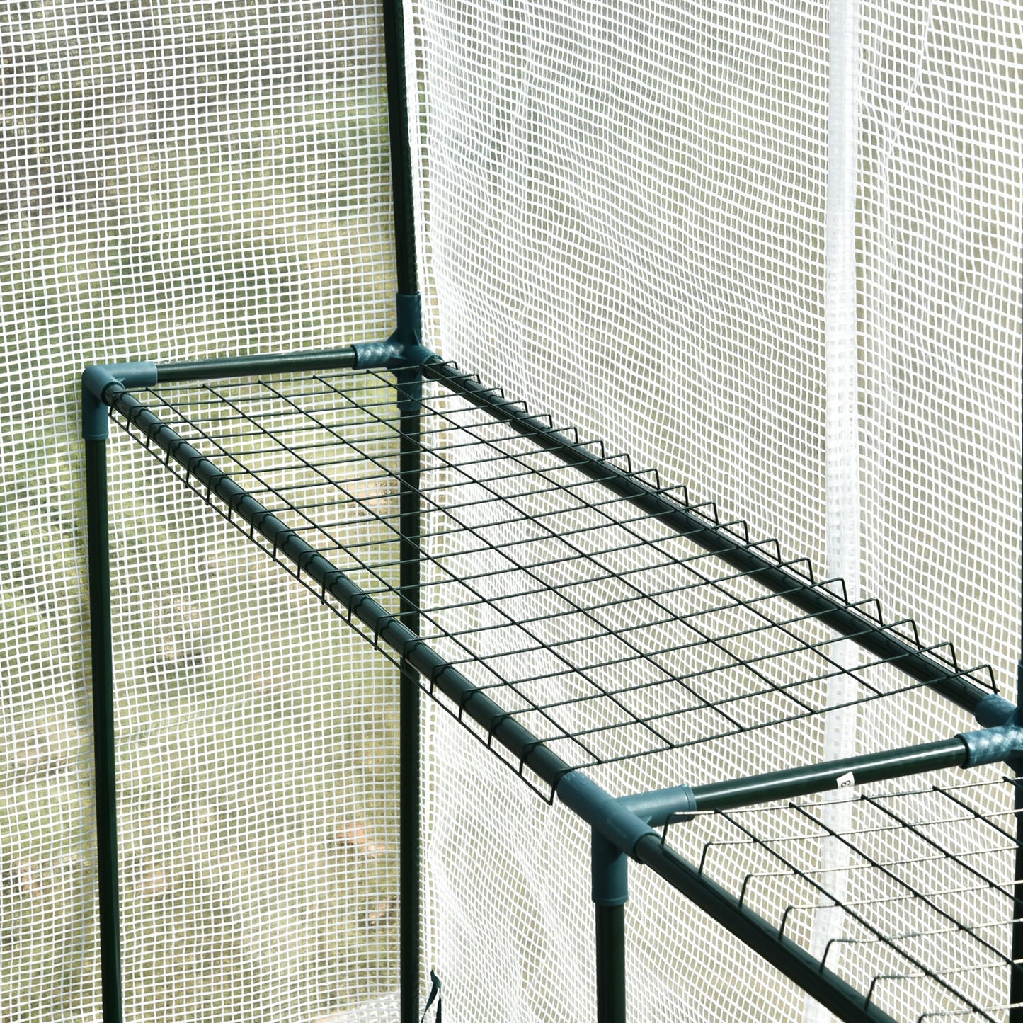 Closeup of a green metal frame with wire shelving inside a greenhouse ready for plants