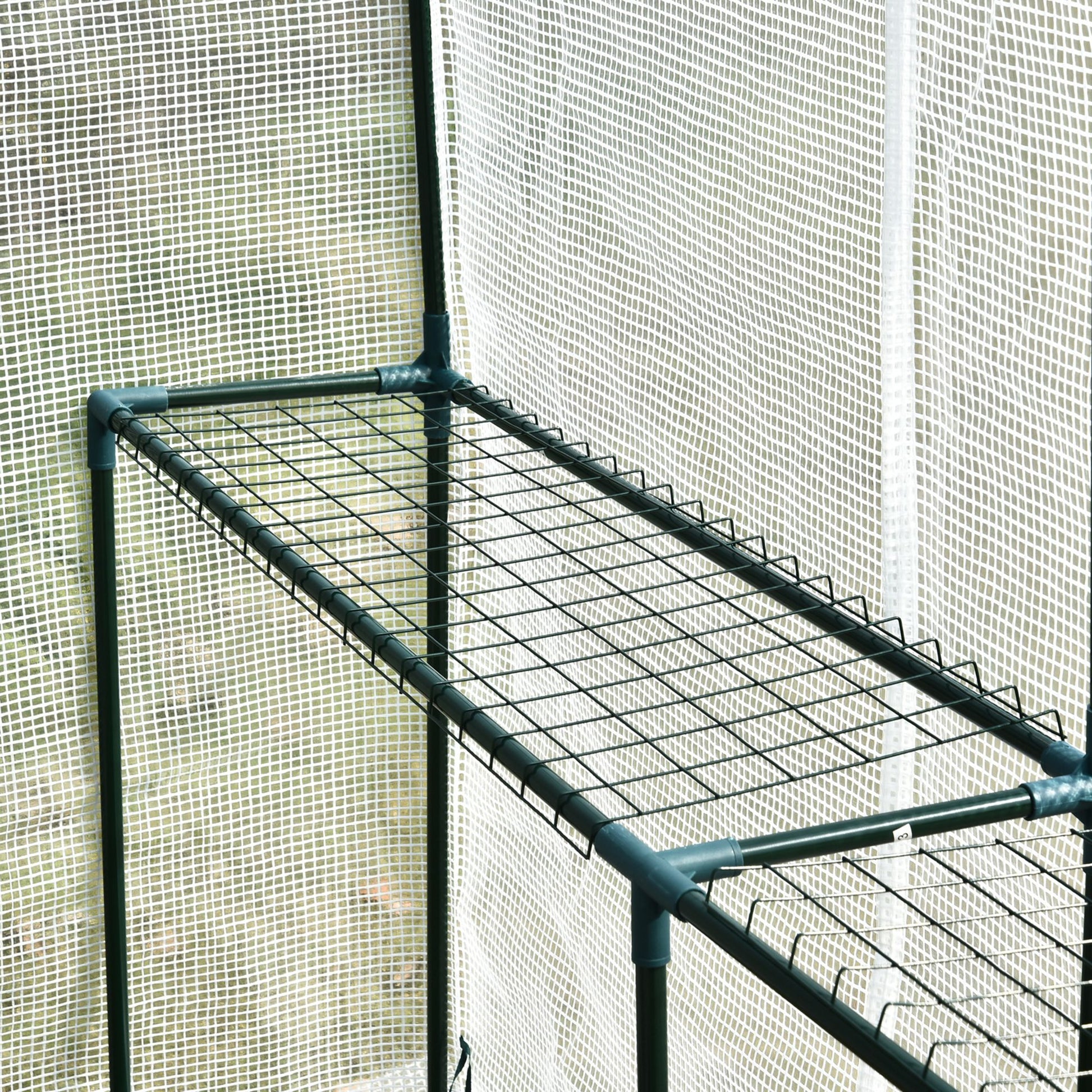 Closeup of a green metal frame with wire shelving inside a greenhouse ready for plants