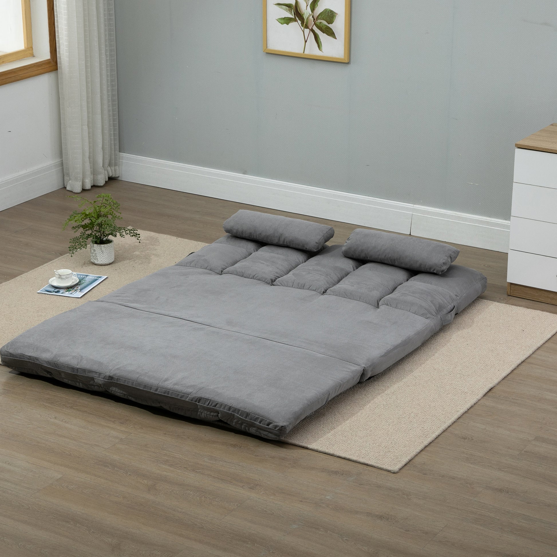 Gray upholstered futon mattress unfolded on floor with two pillows