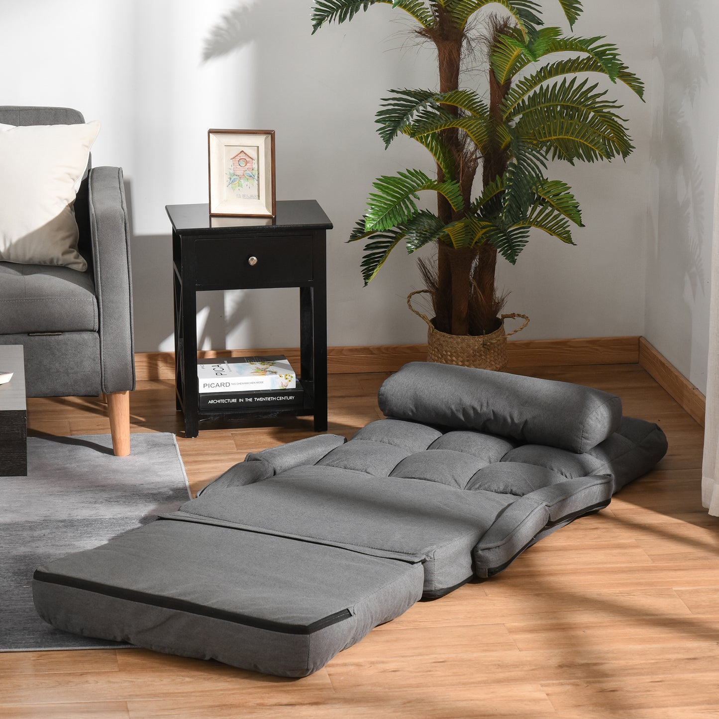 Grey fabric futon sofa bed unfolded featuring tufted cushions and a bolster pillow