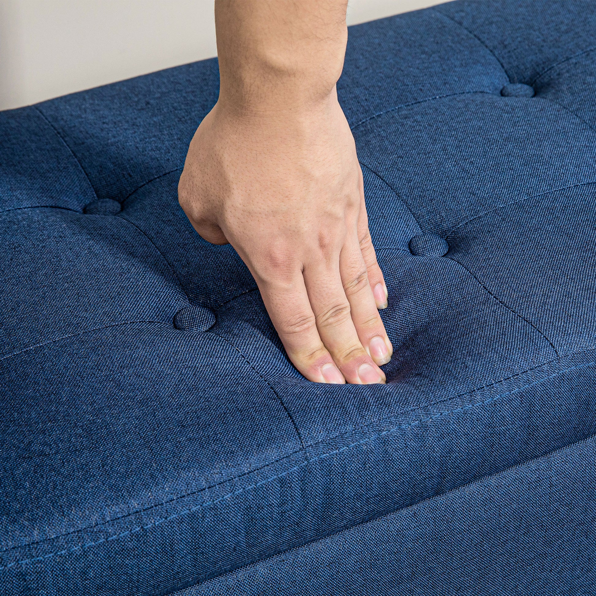 Closeup of hand pressing into deep blue tufted fabric ottoman for comfort test