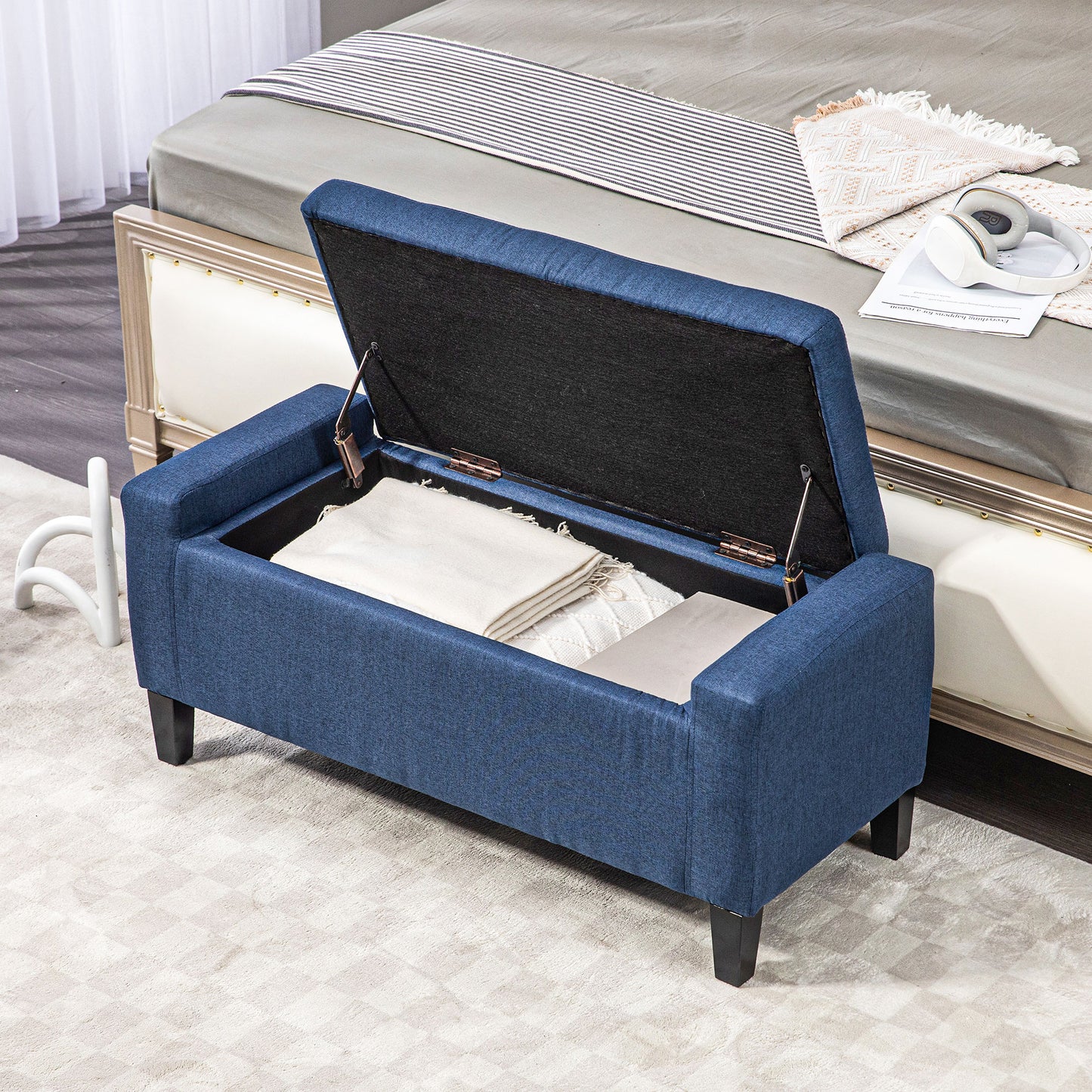 Navy blue upholstered storage bench with hinged lid open showing blankets inside