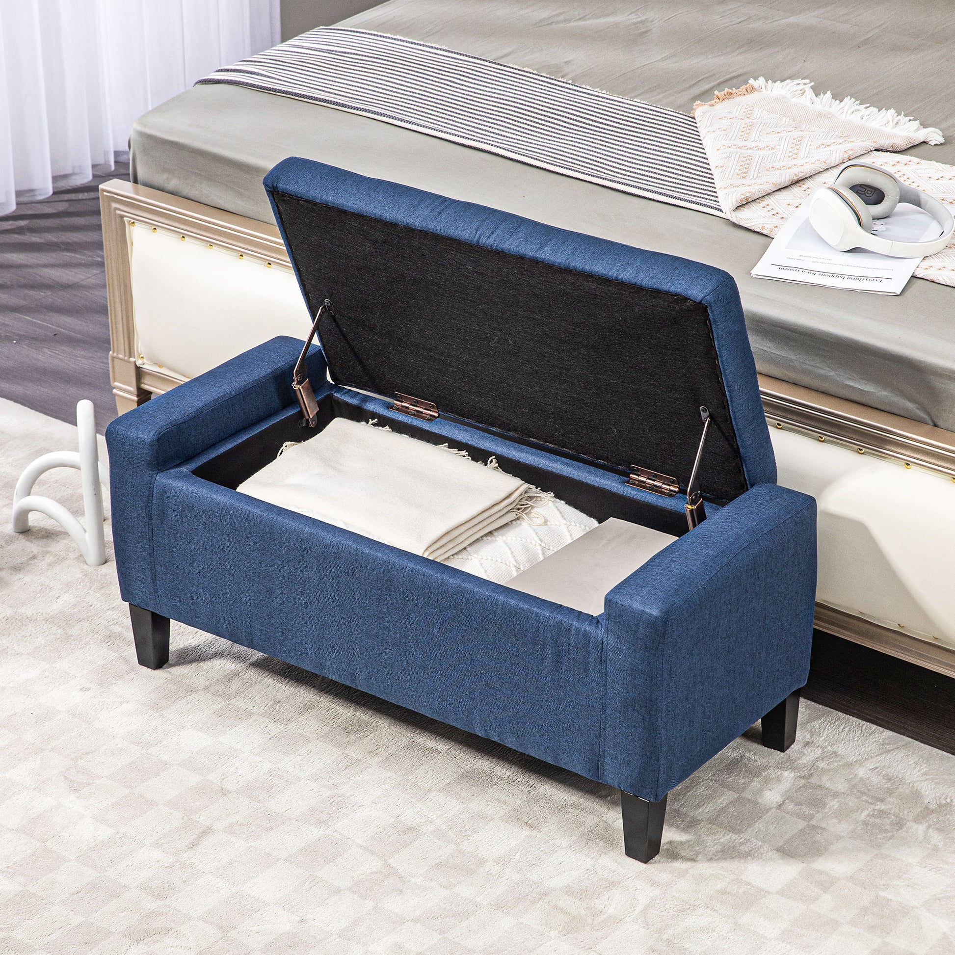 Navy blue upholstered storage bench with hinged lid open showing blankets inside