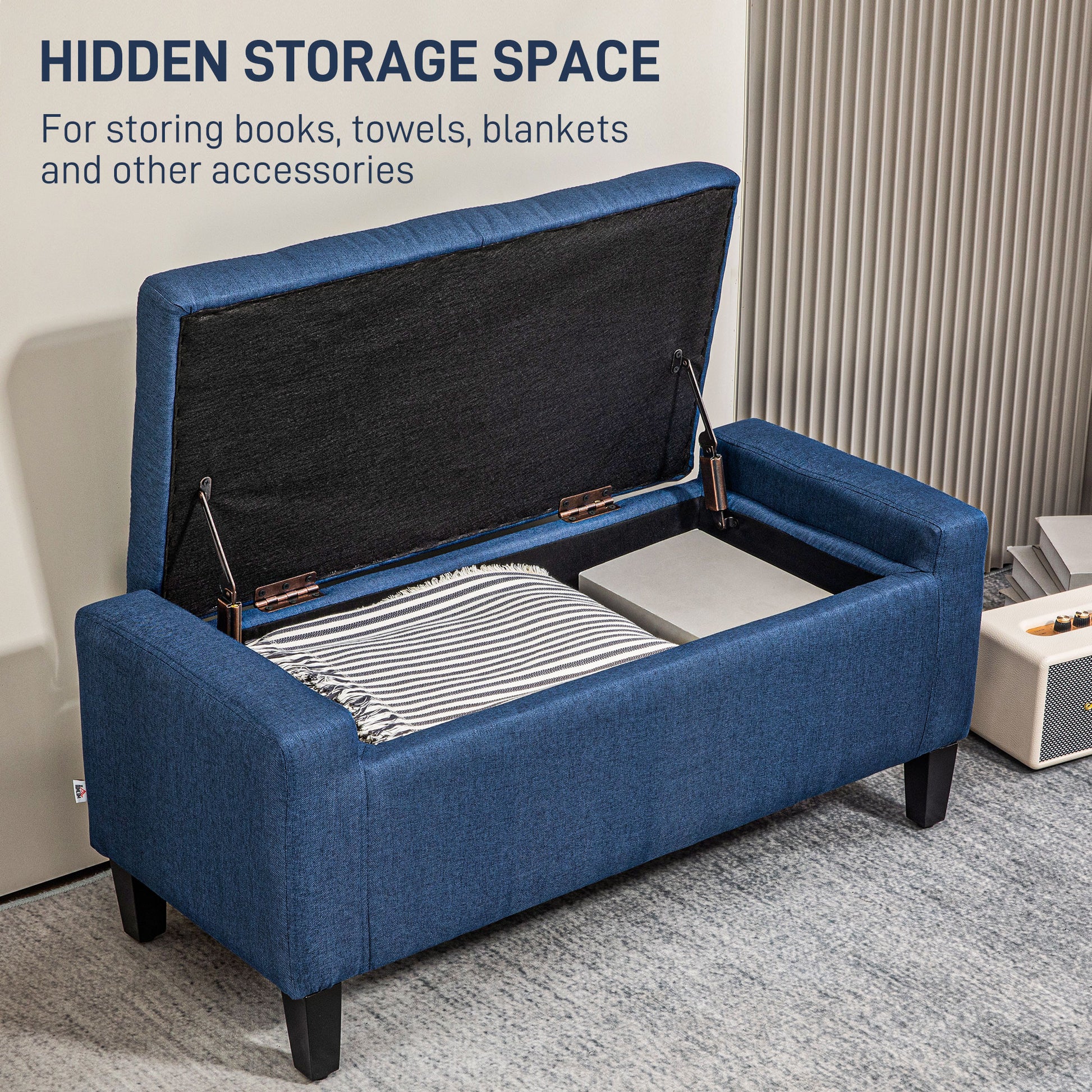 Blue upholstered storage ottoman with lid open revealing books and blankets inside