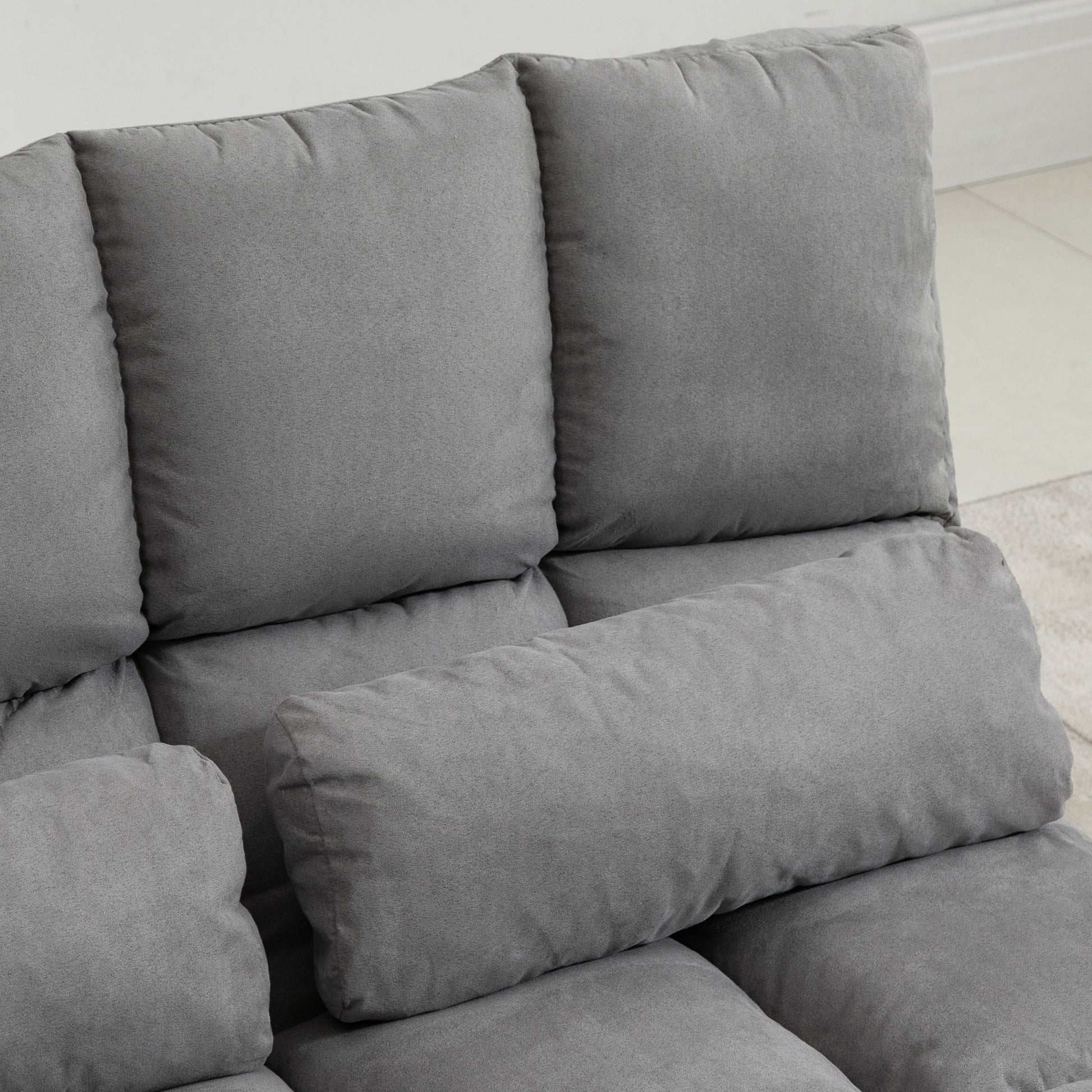 Closeup of a plush grey fabric sofa with multiple cushioned sections and a lumbar pillow