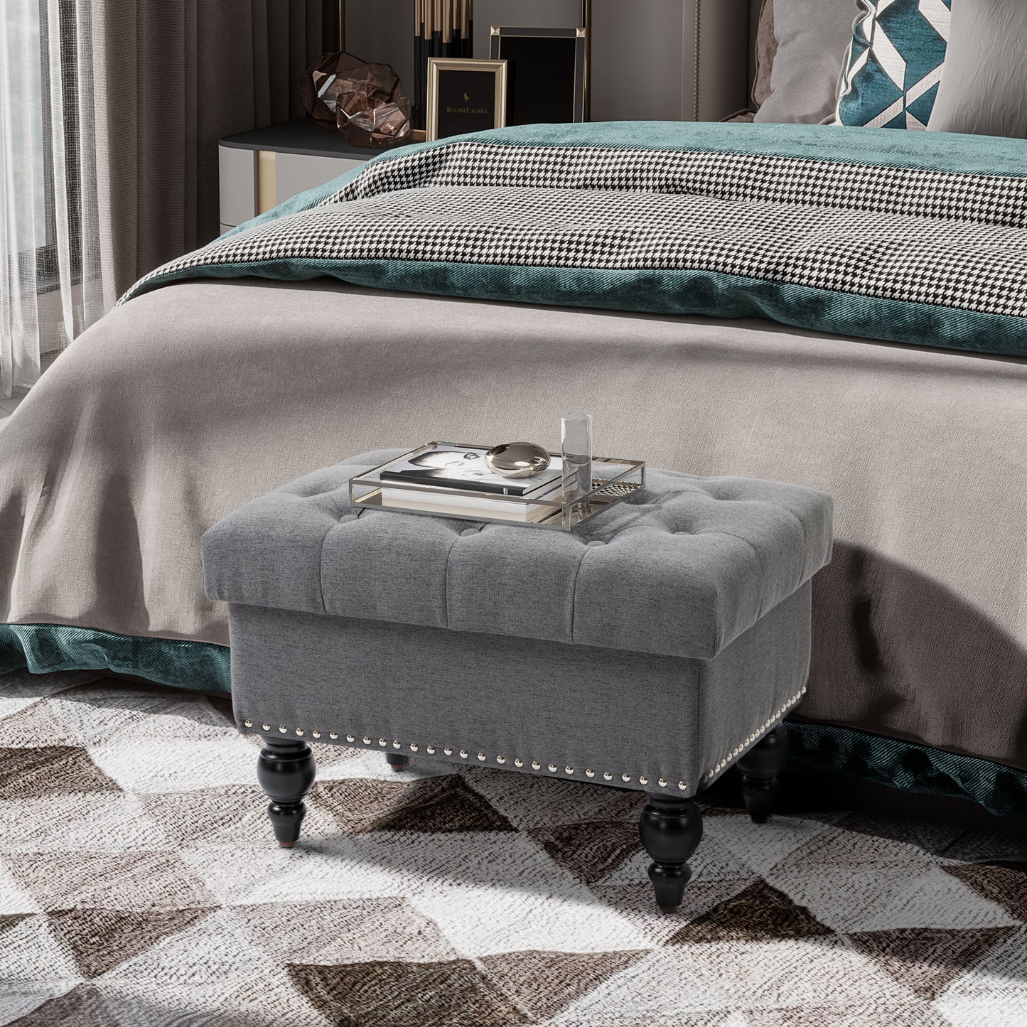 Tufted grey fabric storage ottoman with silver nailhead trim and black carved legs