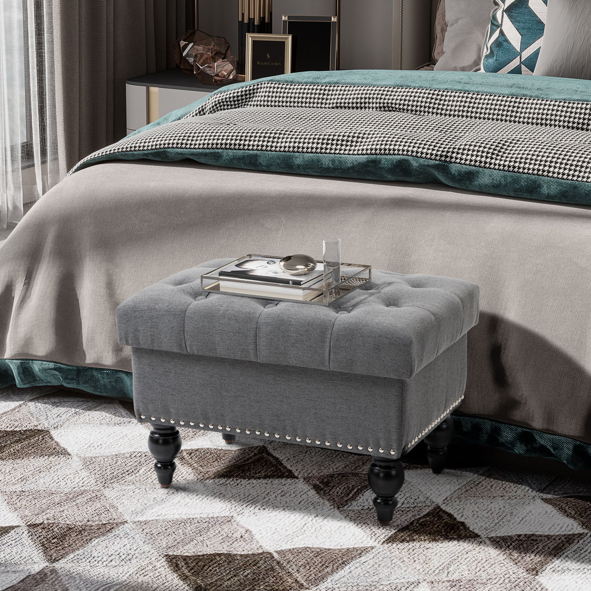 Tufted grey fabric storage ottoman with silver nailhead trim and black carved legs