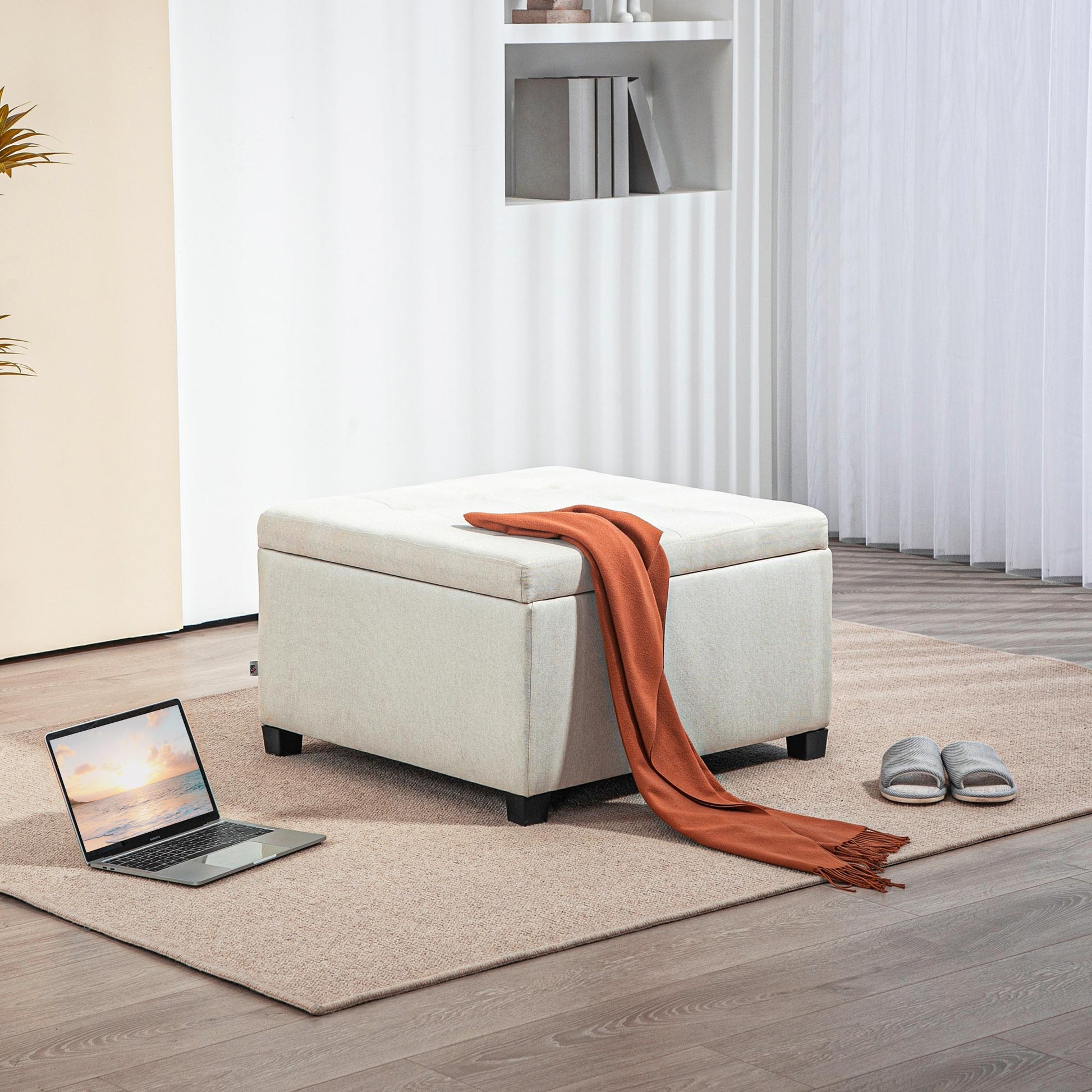 Tufted beige fabric storage ottoman with orange throw blanket on top