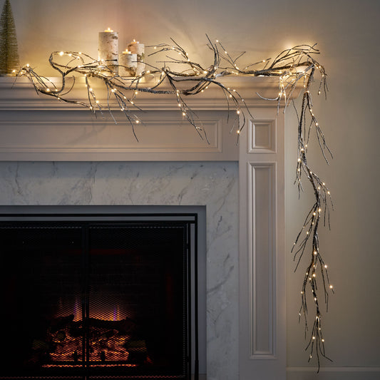 Glittery black branch garland with warm white LED lights draped over a fireplace mantel