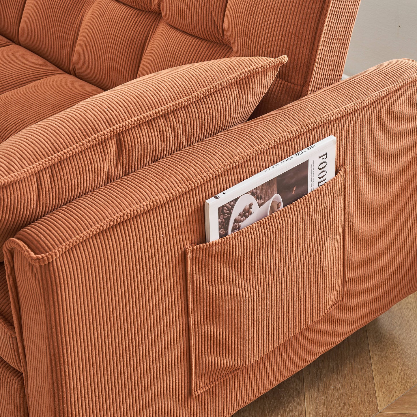 Closeup of plush orange corduroy sofa with tufted cushions and side pocket holding a magazine