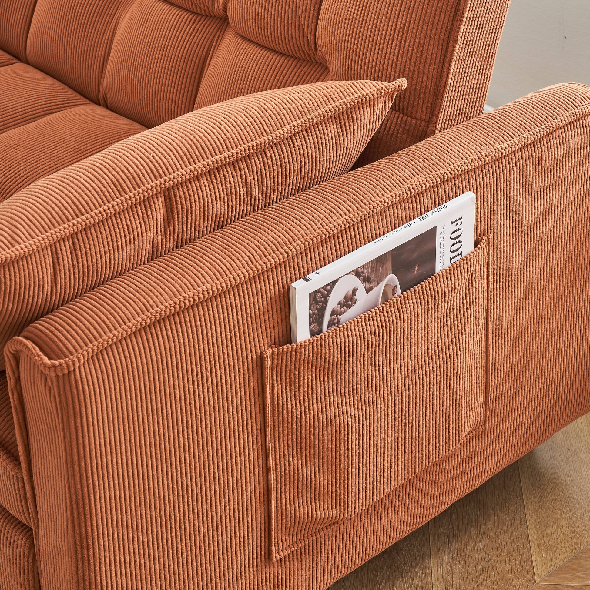 Closeup of plush orange corduroy sofa with tufted cushions and side pocket holding a magazine