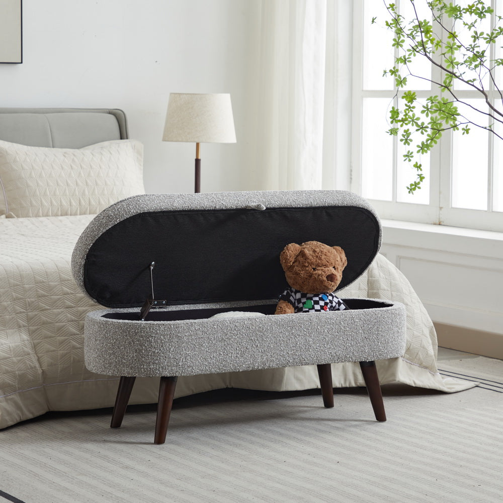 Oval storage ottoman with gray textured fabric and wooden legs open lid revealing teddy bear