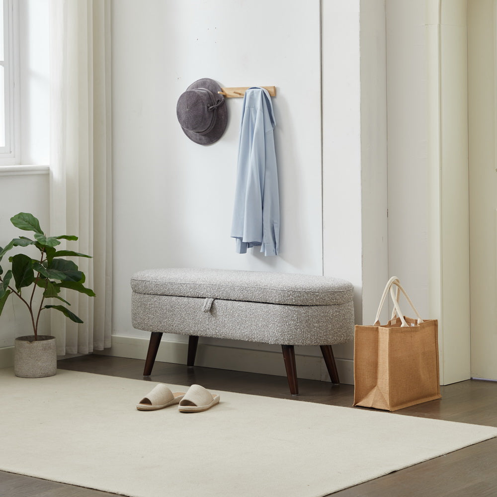 Gray tufted storage ottoman with wooden legs and open lid ideal for entryway organization