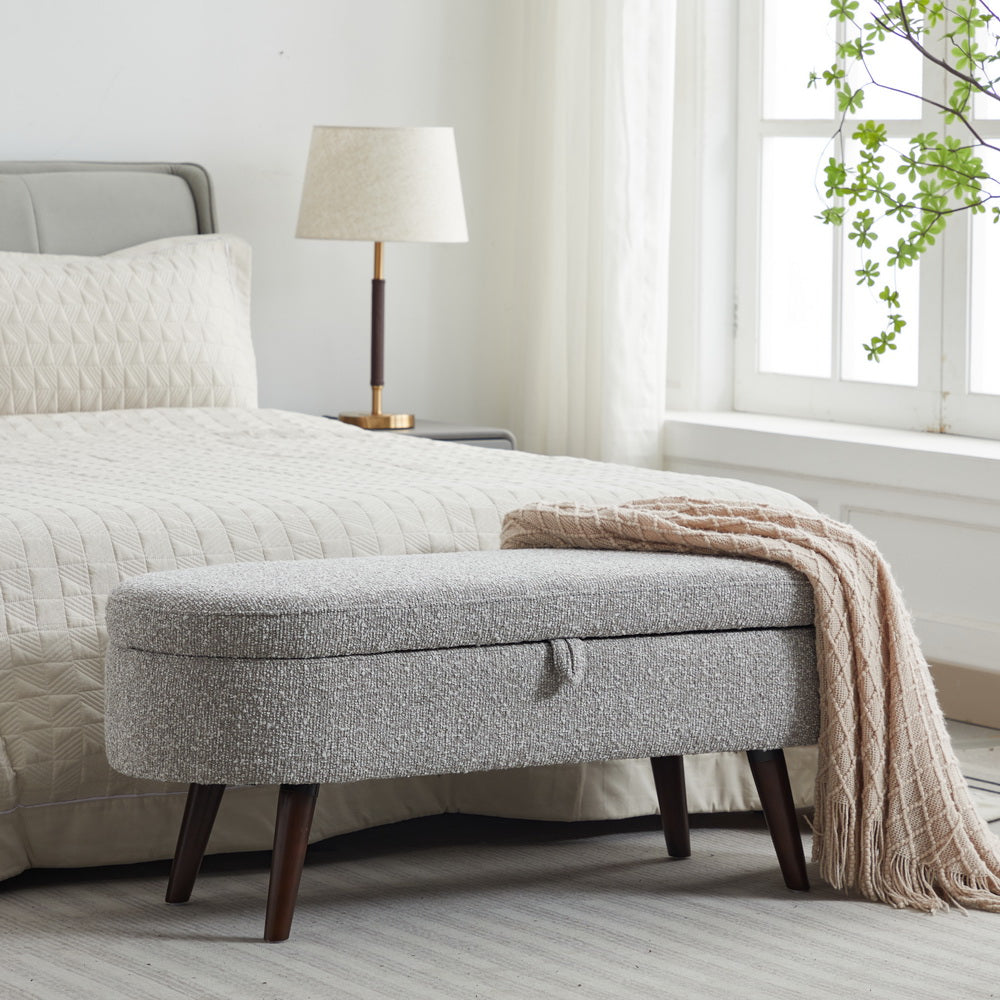 Grey fabric storage bench with dark wooden legs and a knitted throw