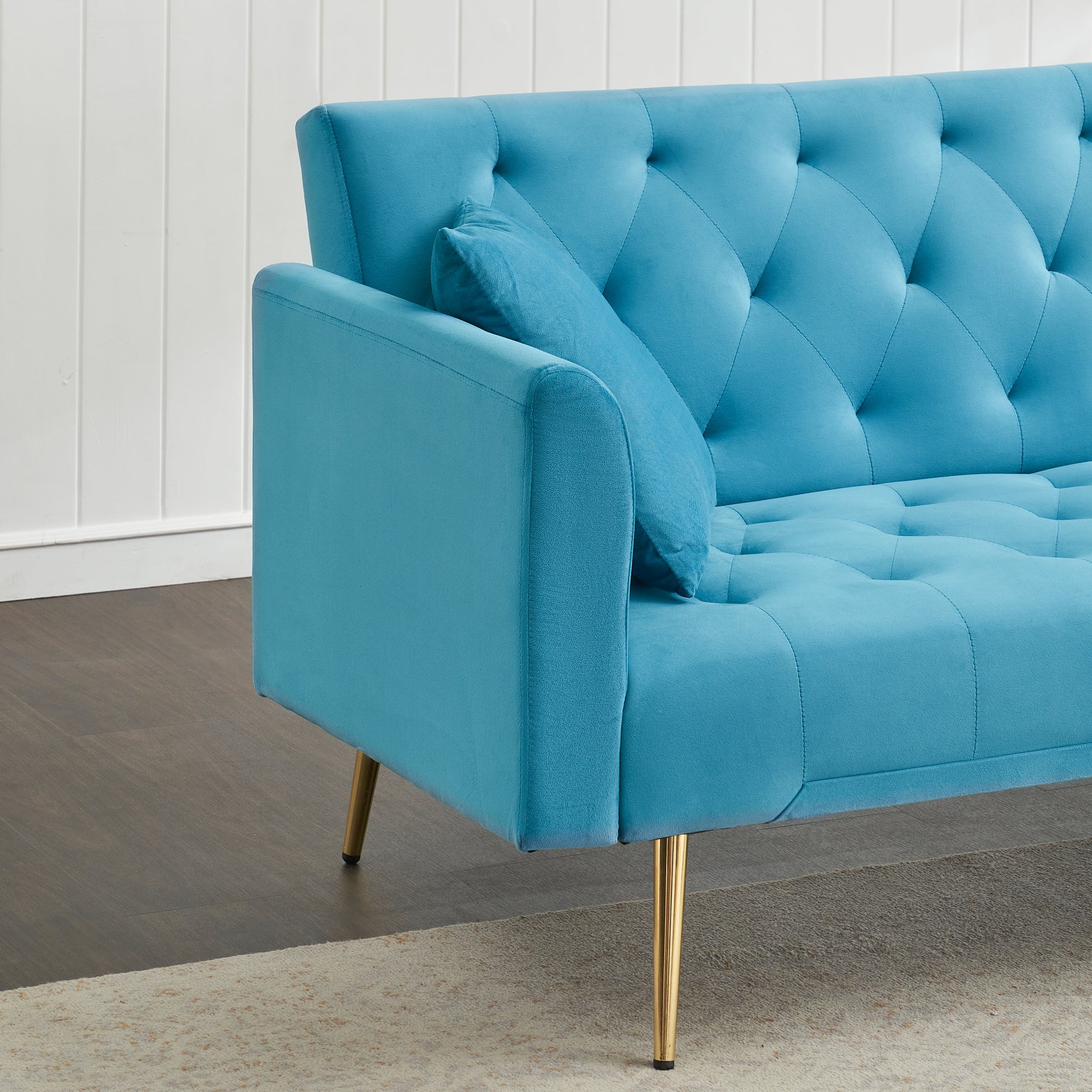 Tufted velvet sofa in bright blue with gold legs and a decorative pillow