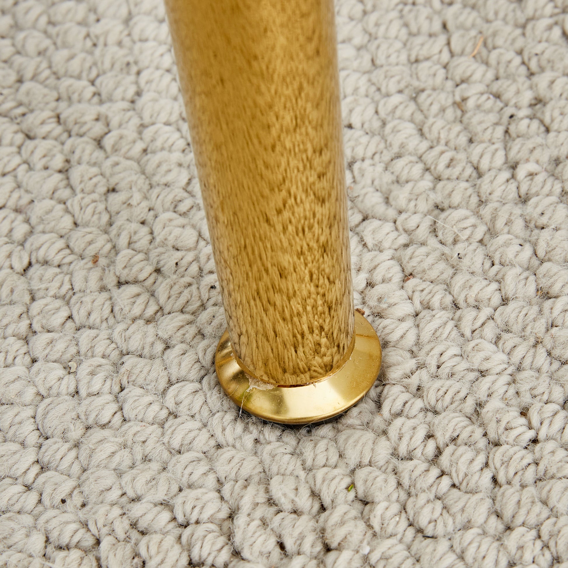 Closeup of a polished brass furniture leg with textured wood grain resting on a light grey rug