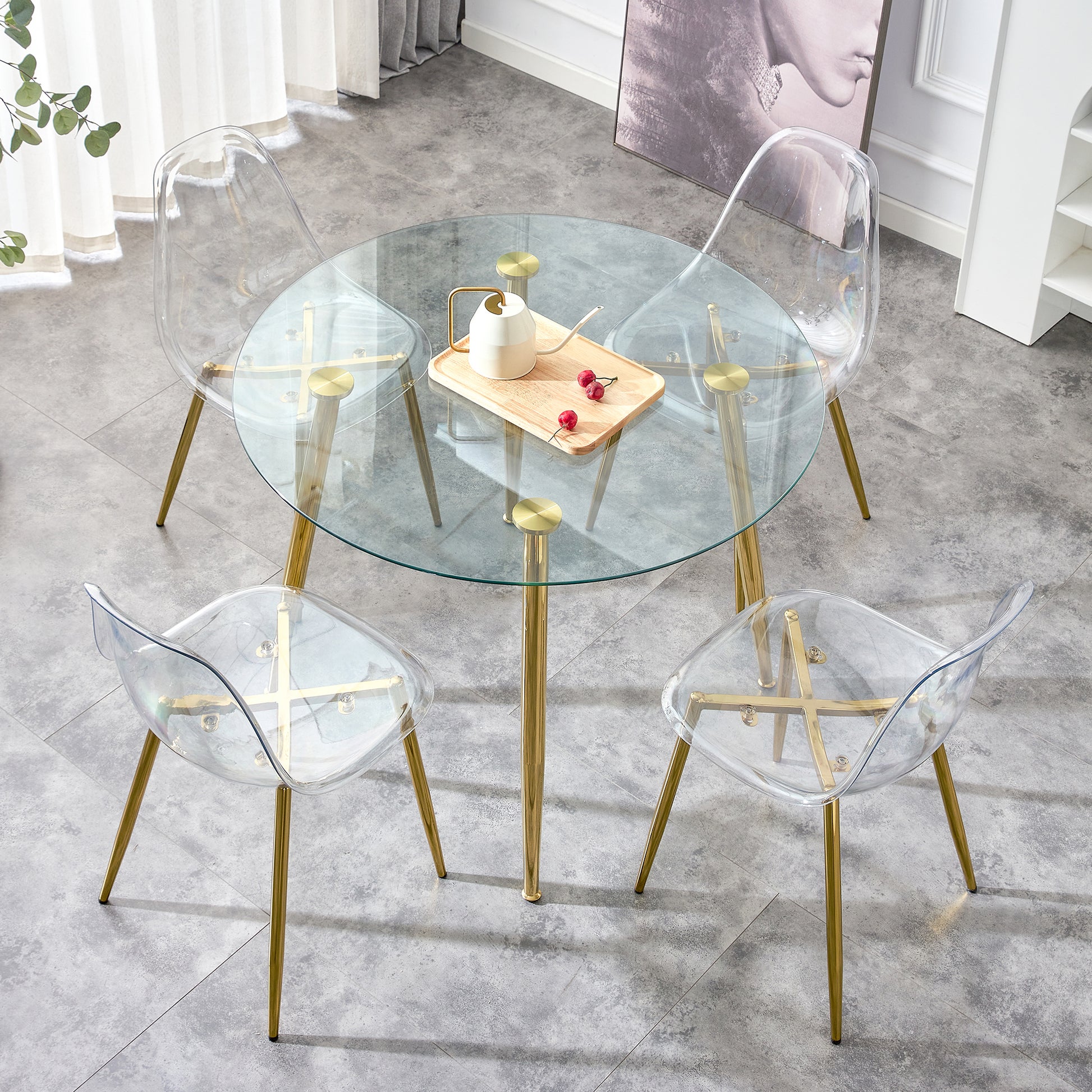 Round glass dining table with gold legs featuring four clear acrylic chairs