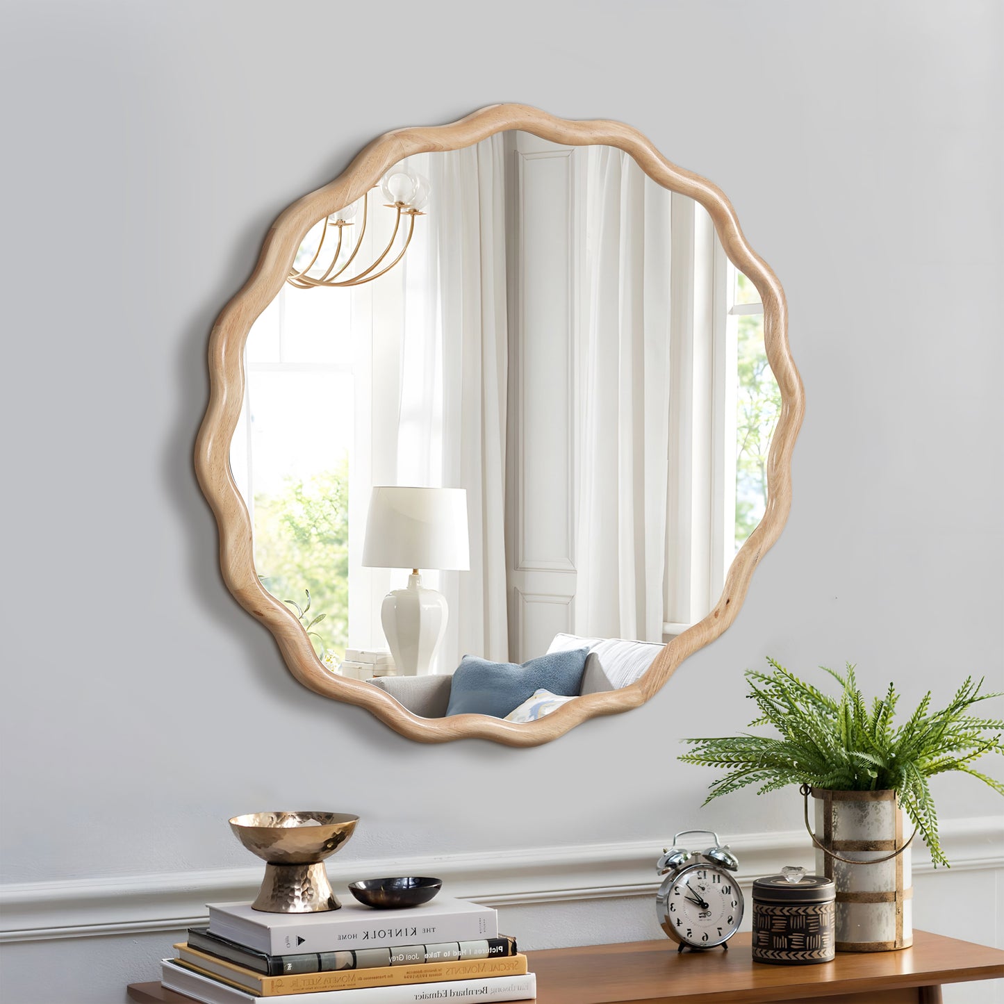 Scalloped wooden framed mirror with a natural finish reflecting a lamp and window