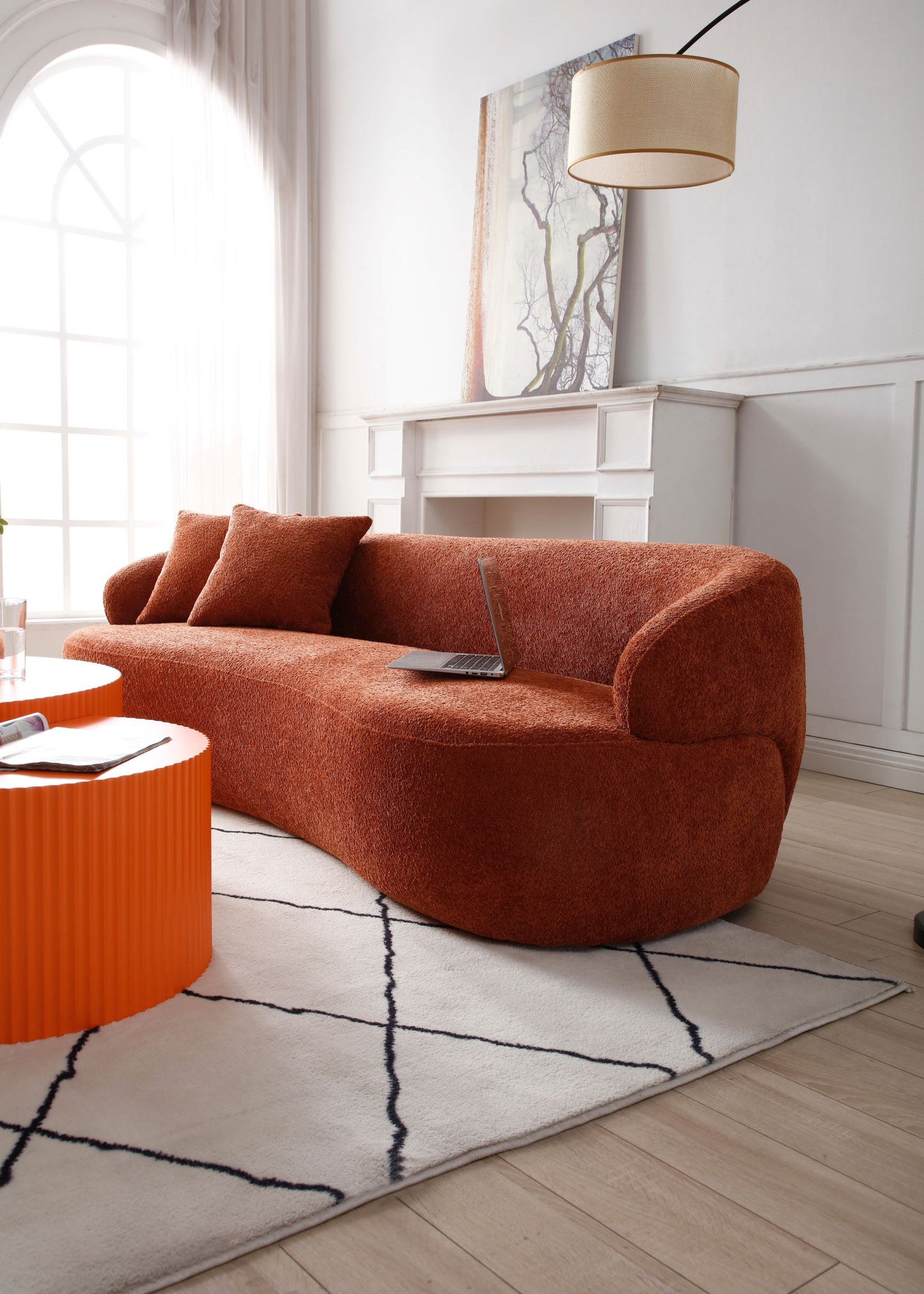 Curved burnt orange boucle sofa with throw pillows and a laptop