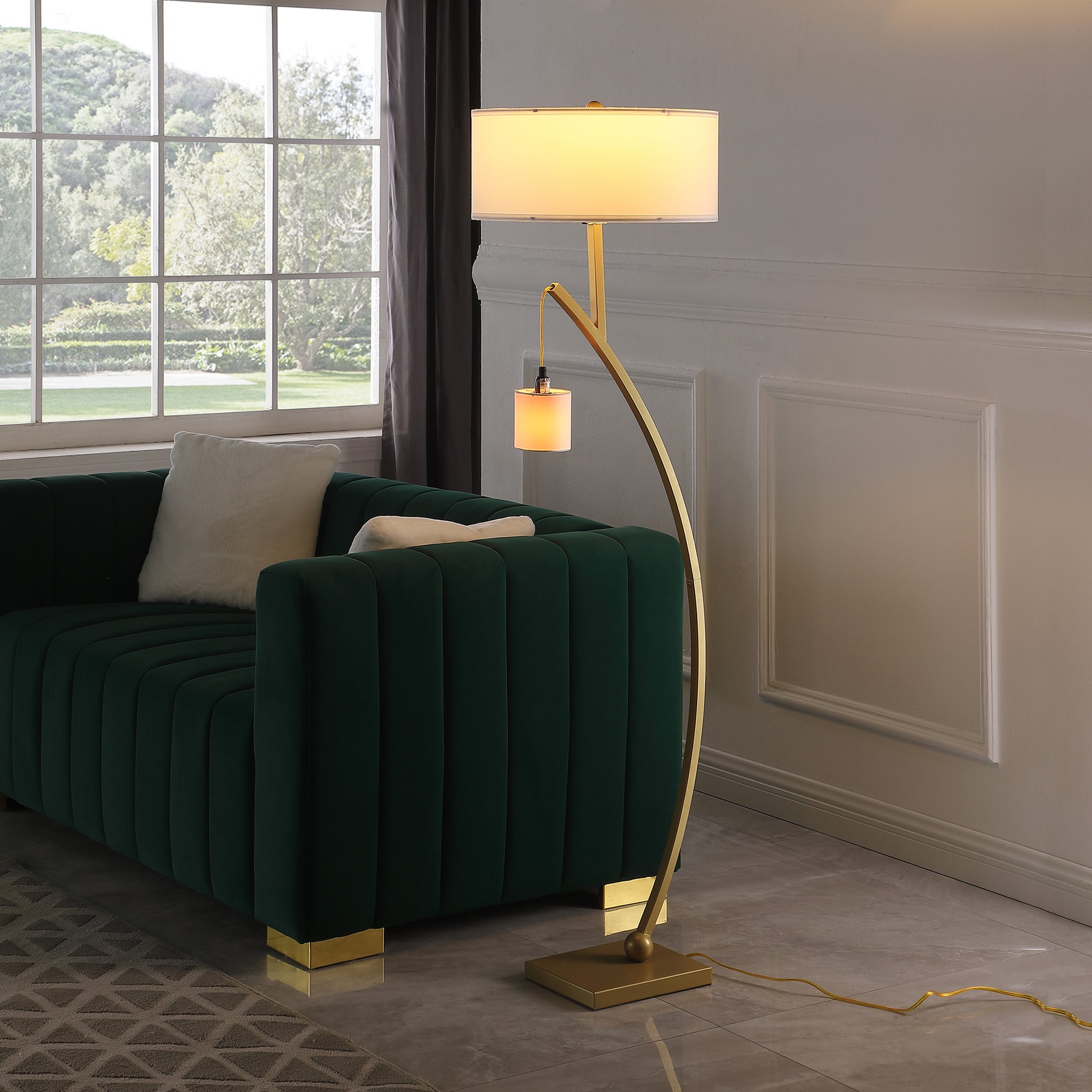 Elegant gold arc floor lamp with dual shades illuminating a plush green sofa