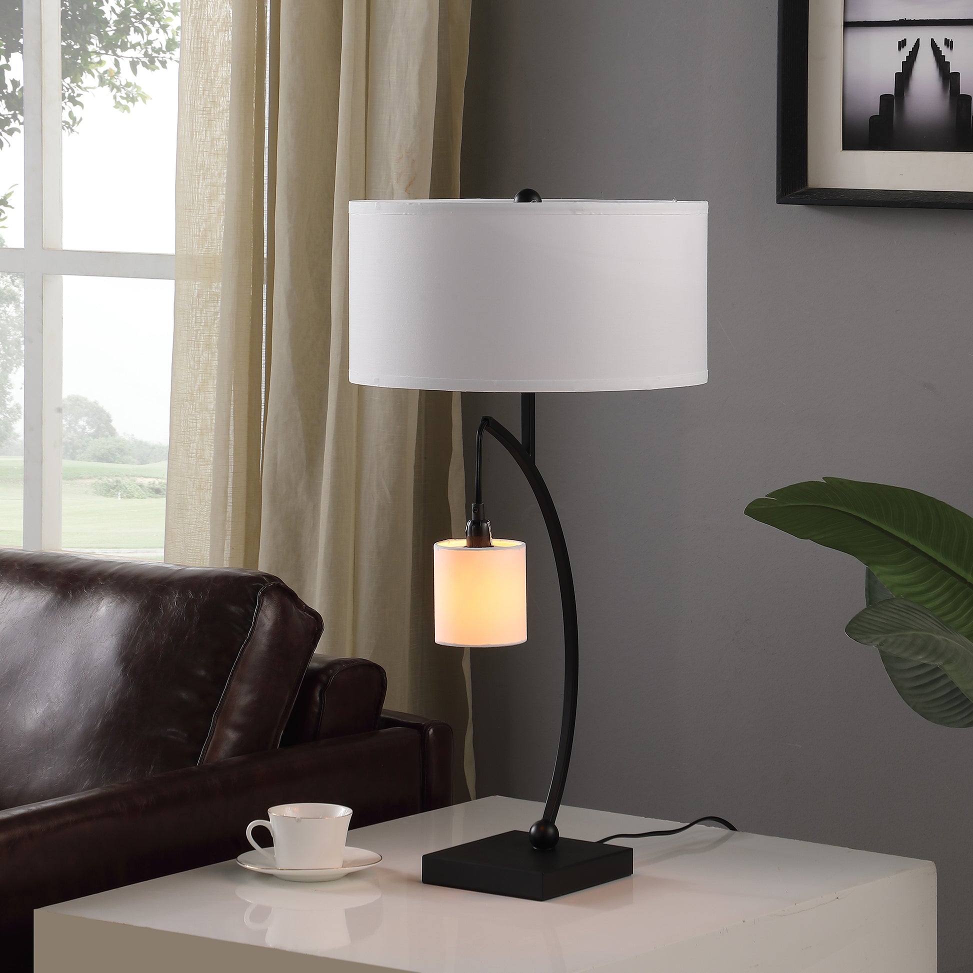 Black modern desk lamp with white drum shade and curved arm holding accent light