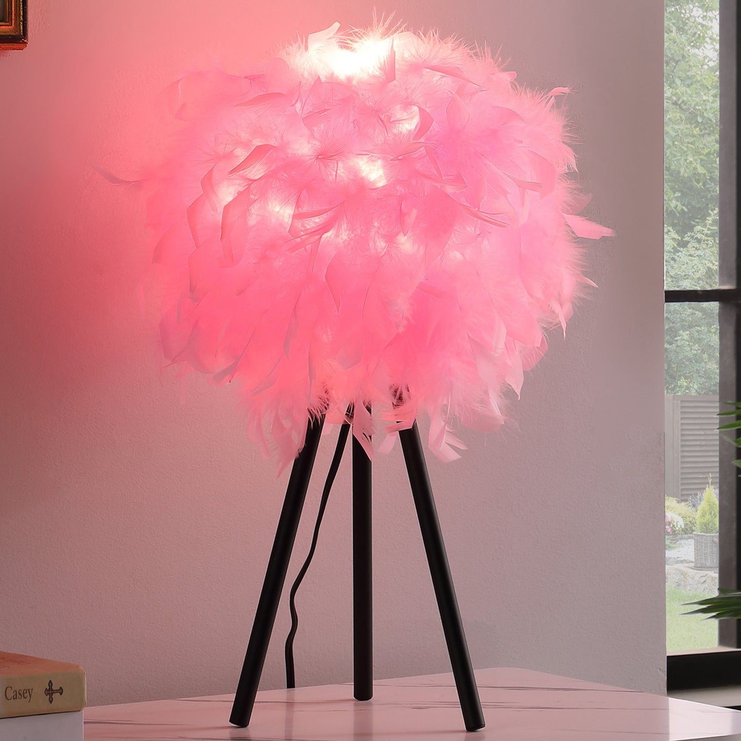 Pink feather table lamp with black tripod base and soft glow