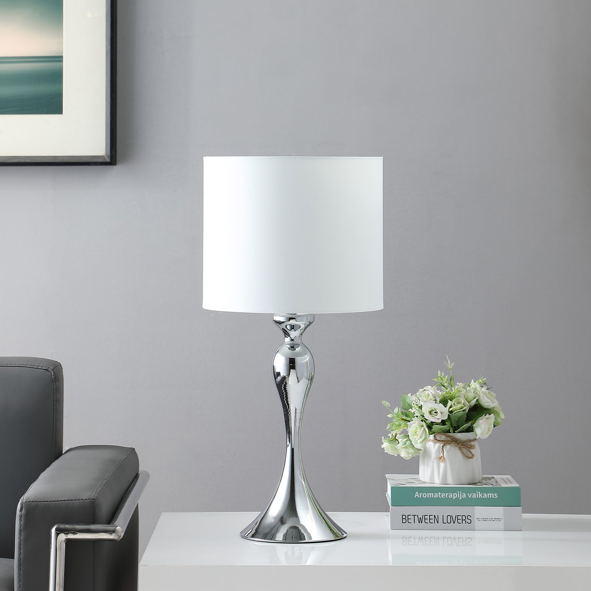 Modern chrome table lamp with a sleek curved base and a white fabric shade perfect for bedside illumination