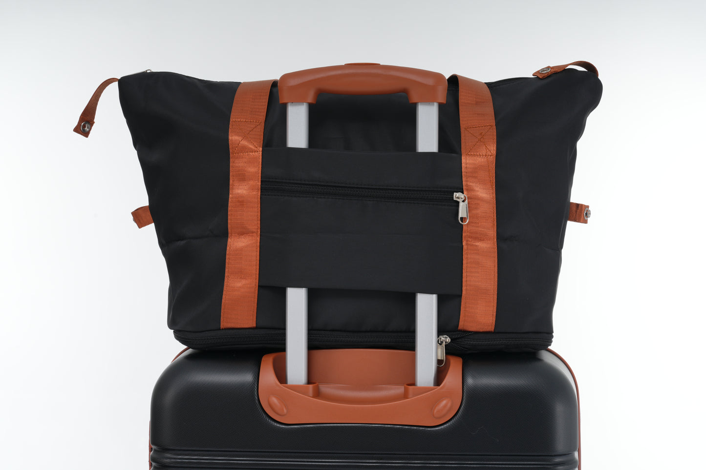 Black duffel bag with orange straps stacked on a black suitcase for travel