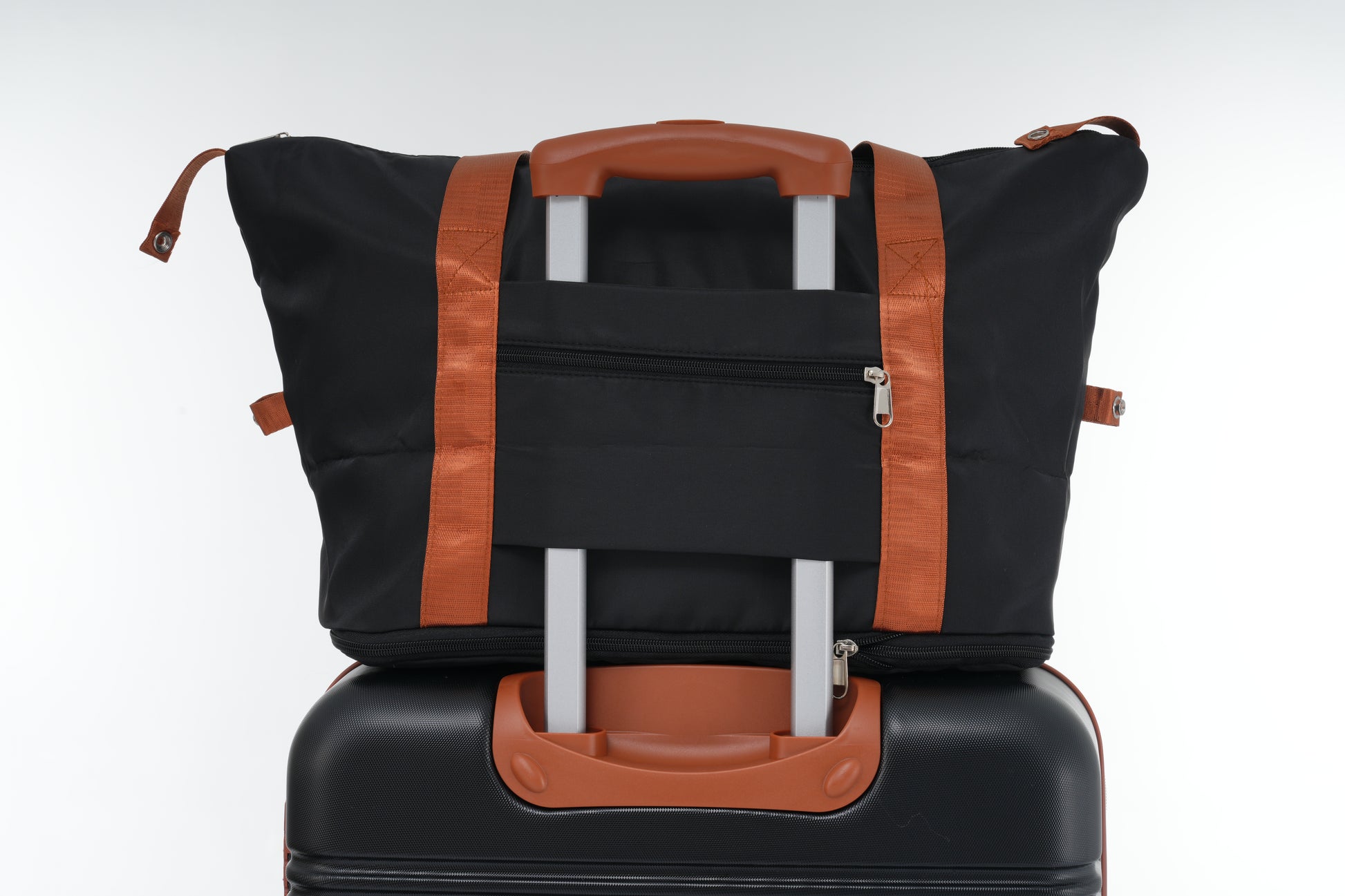 Black duffel bag with orange straps stacked on a black suitcase for travel