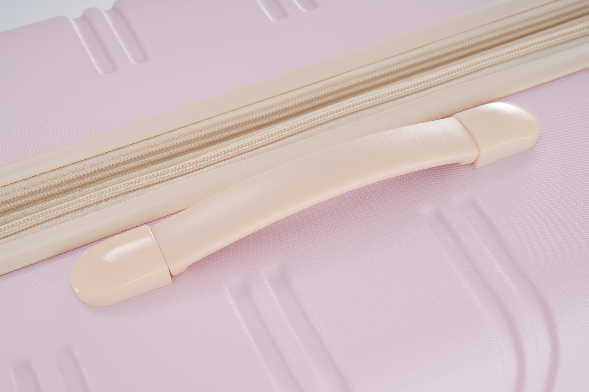 Closeup of a pink suitcase with beige zipper and handle details