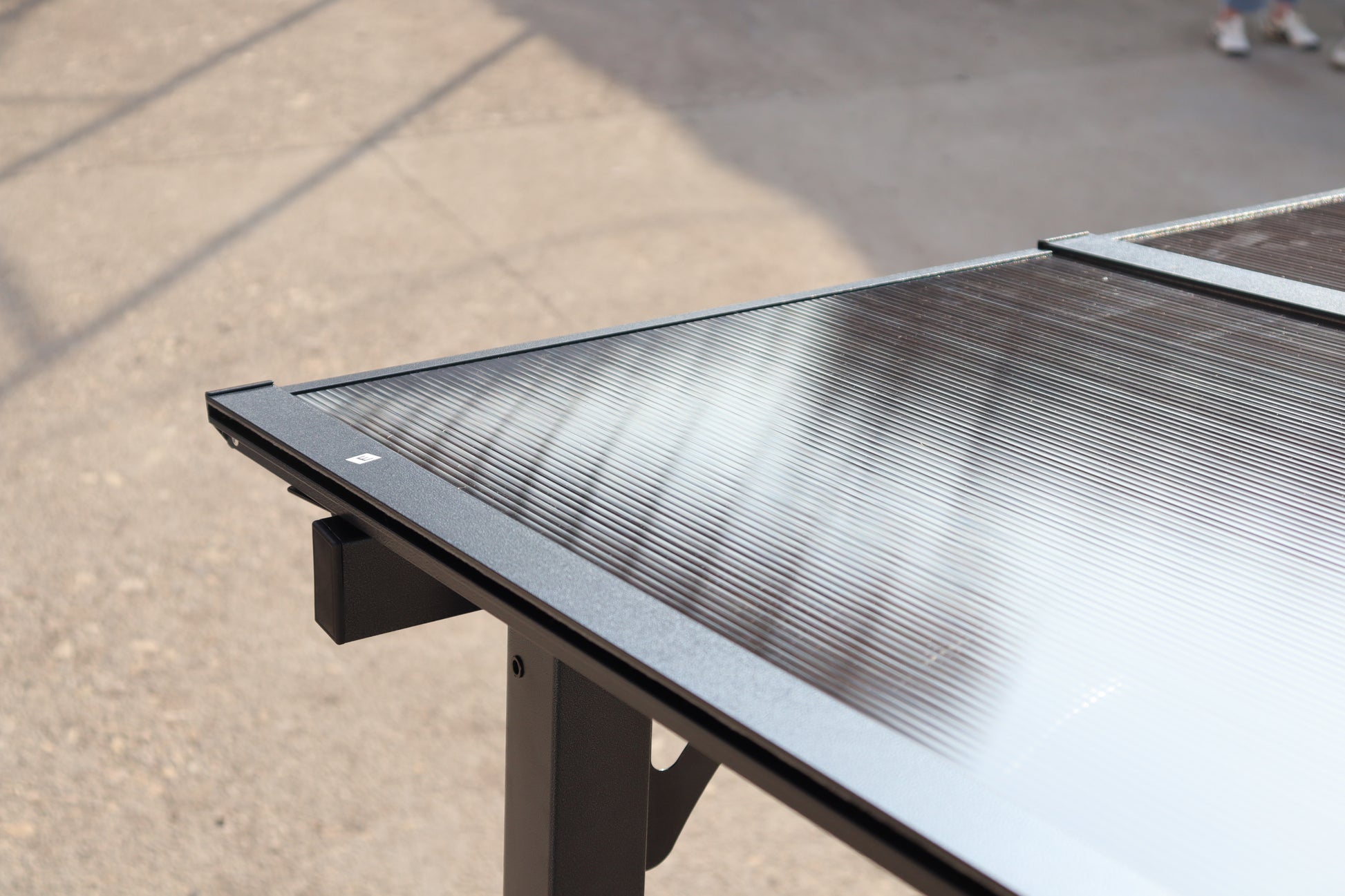 Closeup of a dark grey metal frame outdoor table with a ribbed polycarbonate top