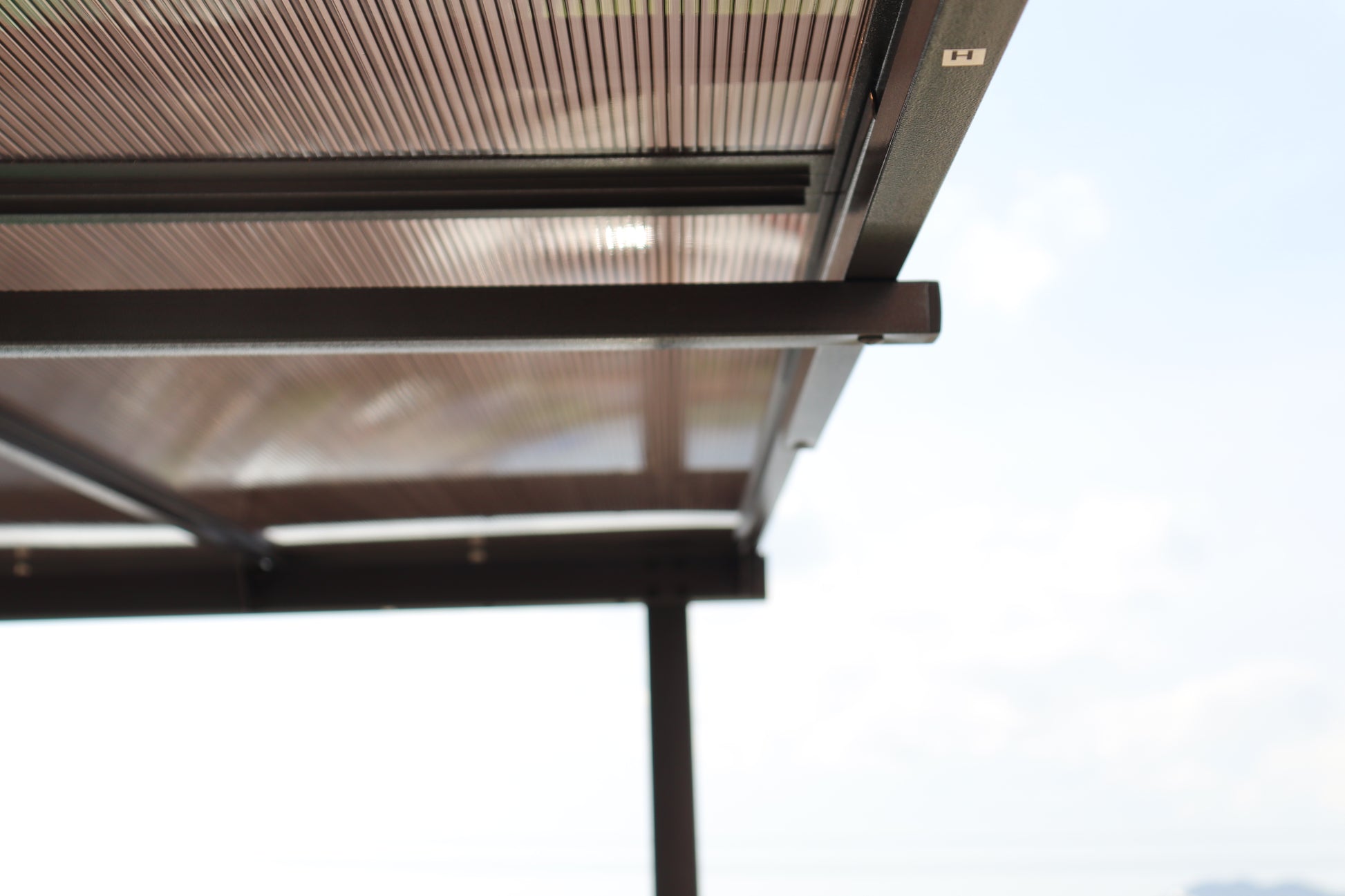 Closeup of a bronze metal patio awning with ridged polycarbonate roofing panels