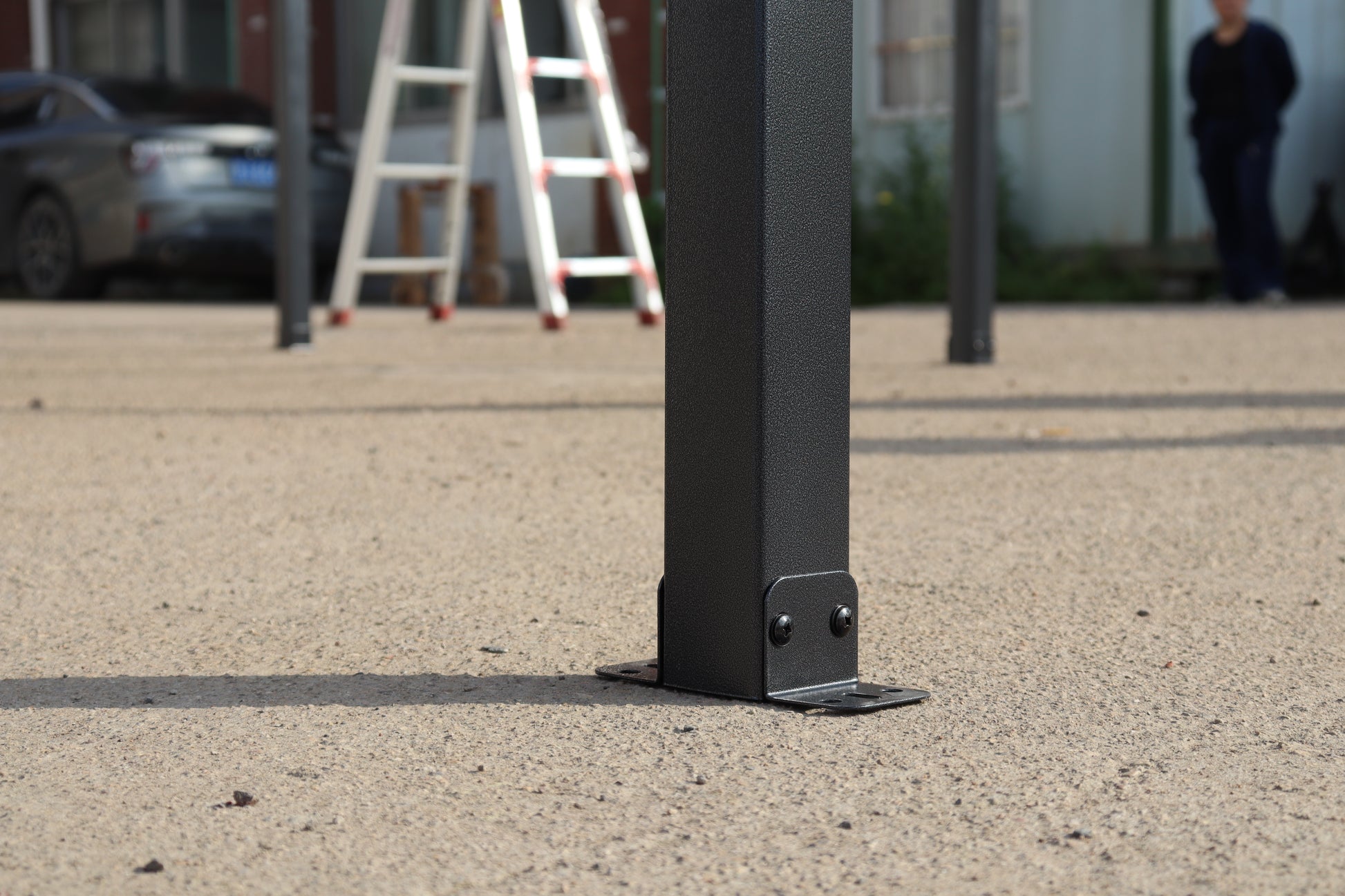 Black textured metal gazebo post with angled metal foot and two screws securing to ground