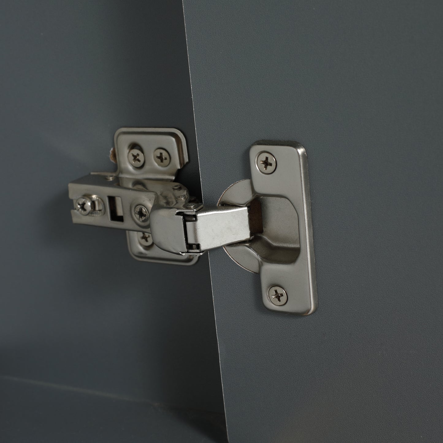 Closeup of a silver cabinet hinge with screws on a dark gray surface