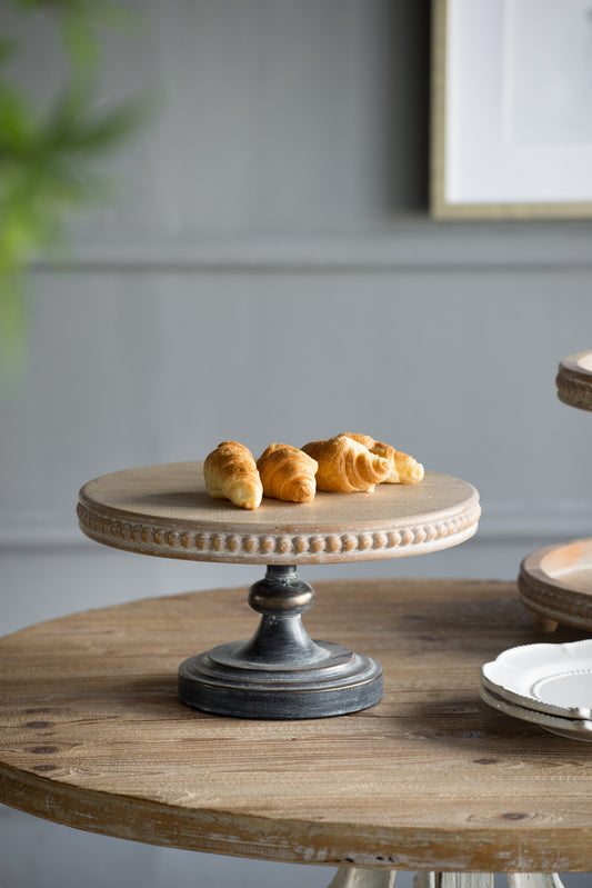 Distressed wood cake stand with beaded edge and antique metal base holding golden croissants