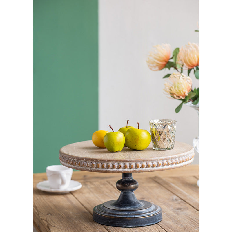 Rustic wooden cake stand with beaded rim displaying decorative apples and a glass
