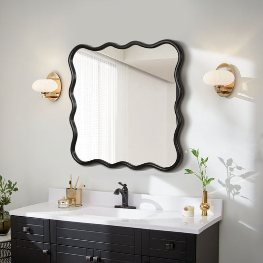 Black wavyedge bathroom mirror with brass sconces and dark vanity