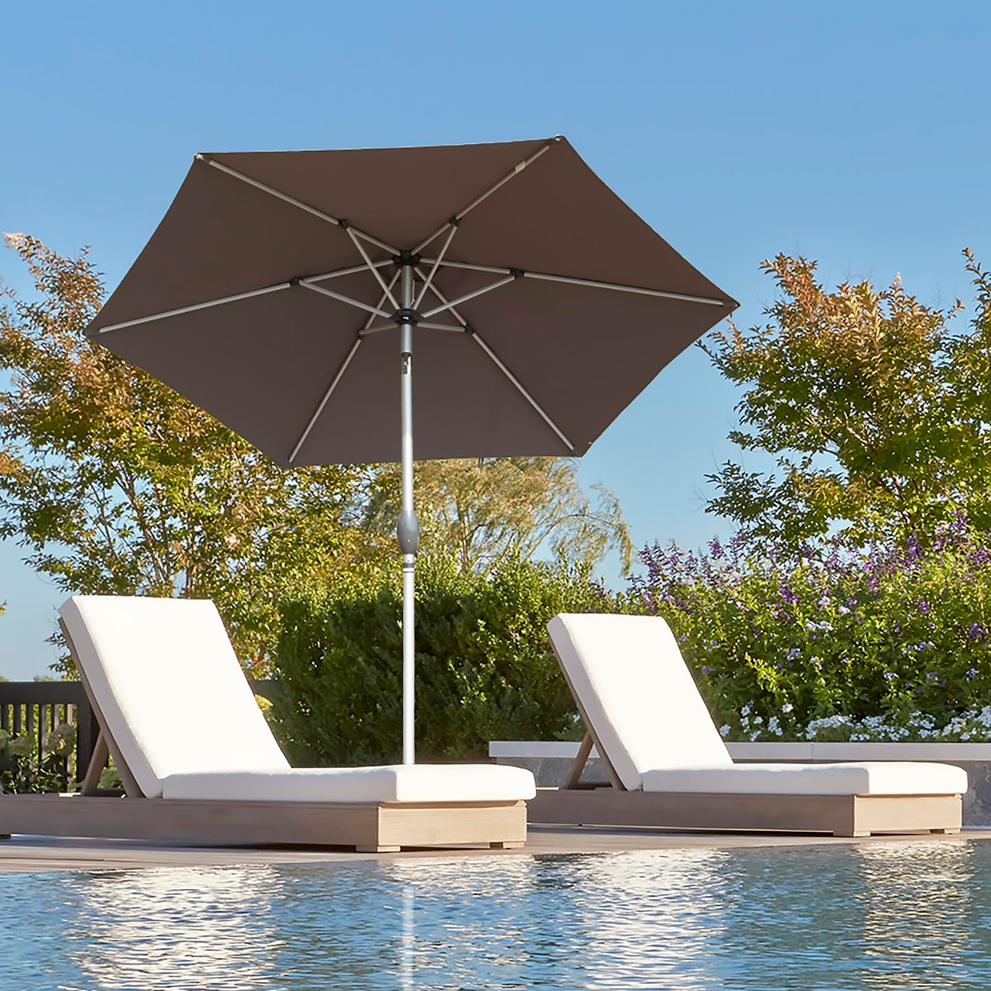 Brown patio umbrella providing shade for two white chaise lounge chairs by a pool