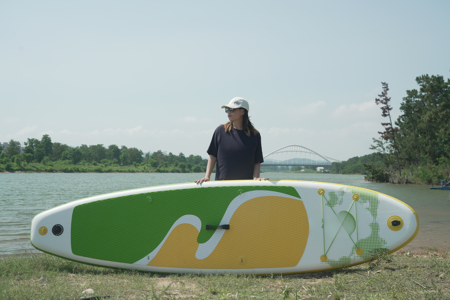 Inflatable stand up paddleboard with green and yellow wave design on a grassy shore