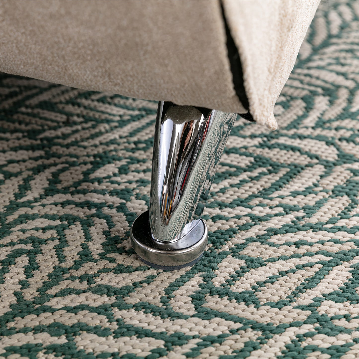 Shiny chrome furniture leg with felt protector on a green and cream chevron rug