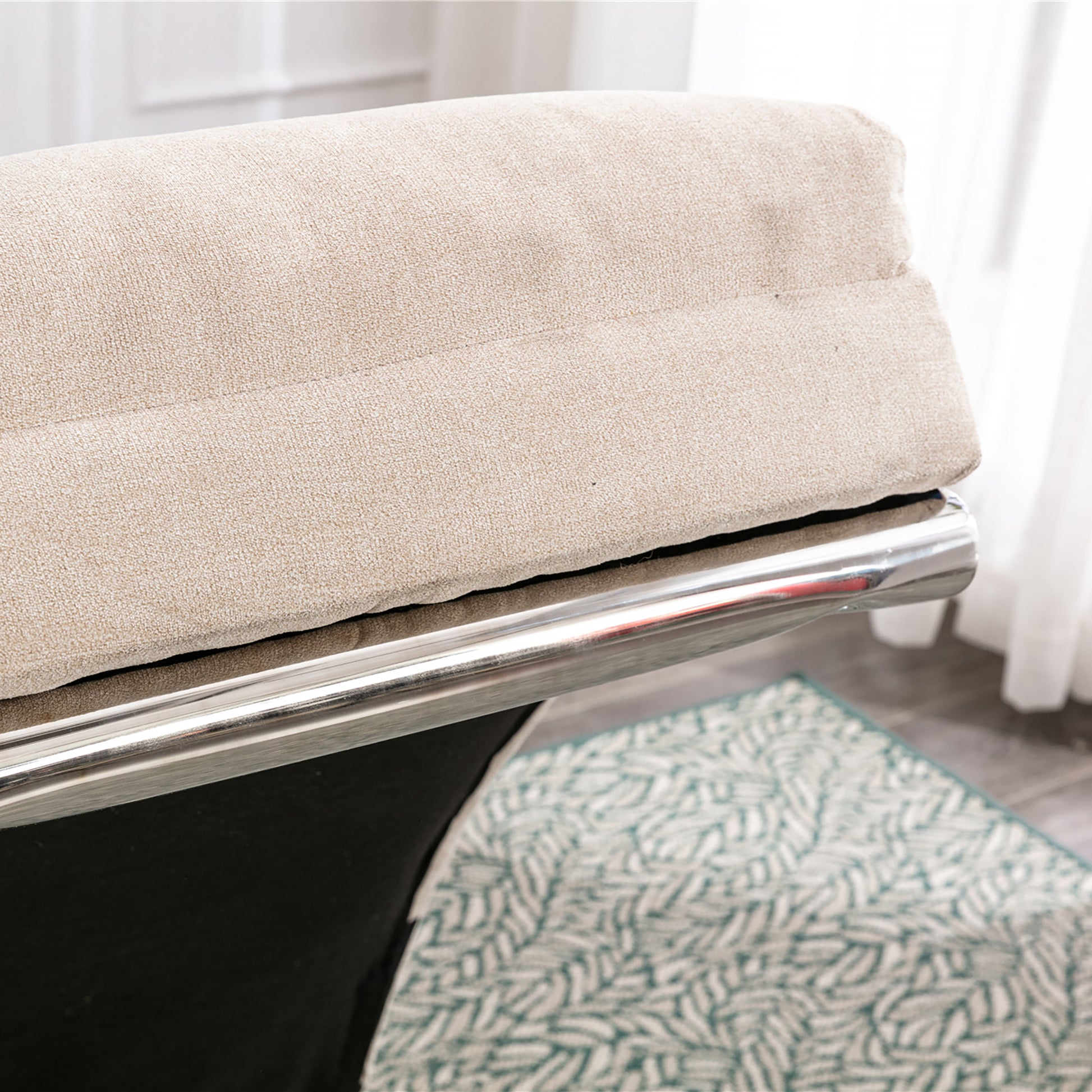 Closeup of a textured beige fabric cushion with a sleek chrome armrest detail on a modern chair