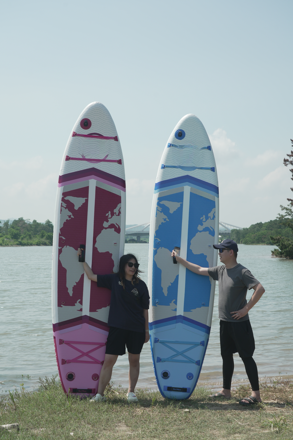Two inflatable stand up paddleboards with world map designs one pink and one blue on a grassy shore