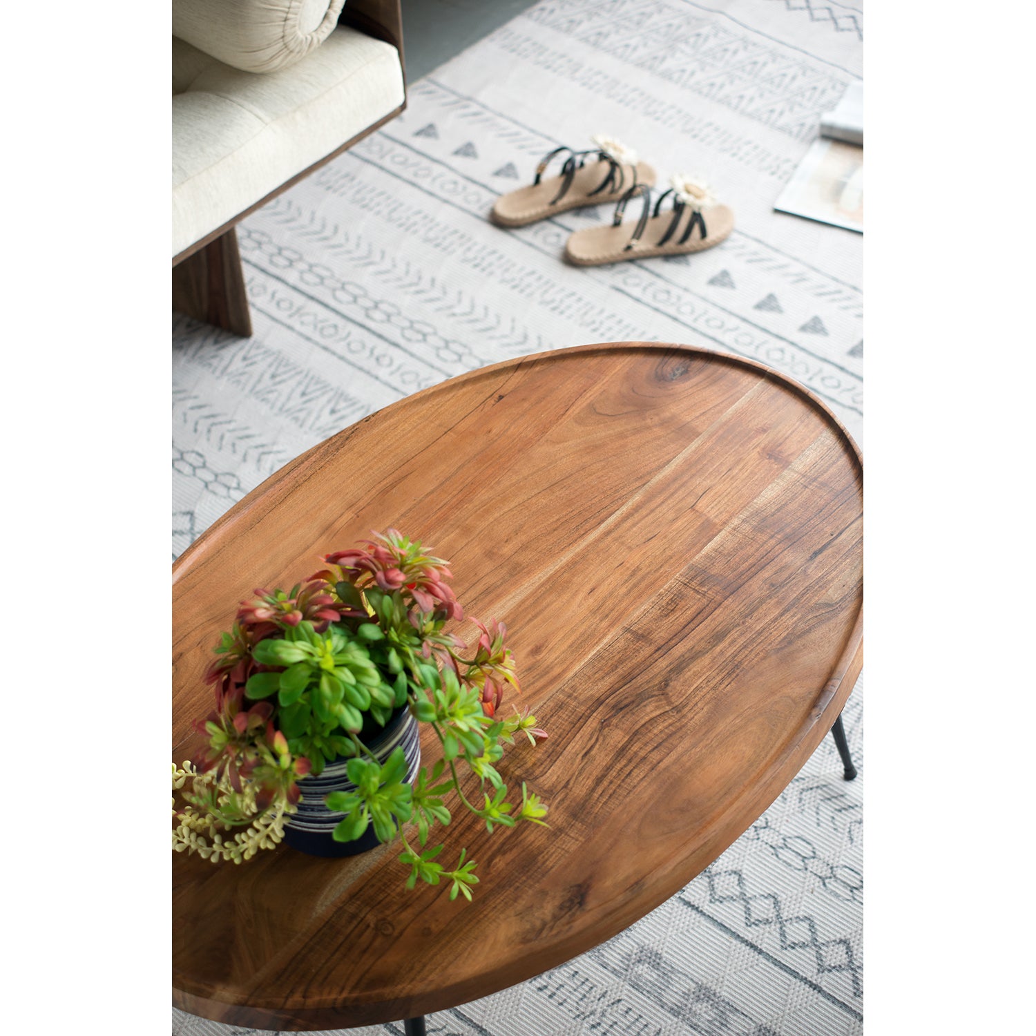 Oval wooden coffee table with plant and slippers on patterned rug