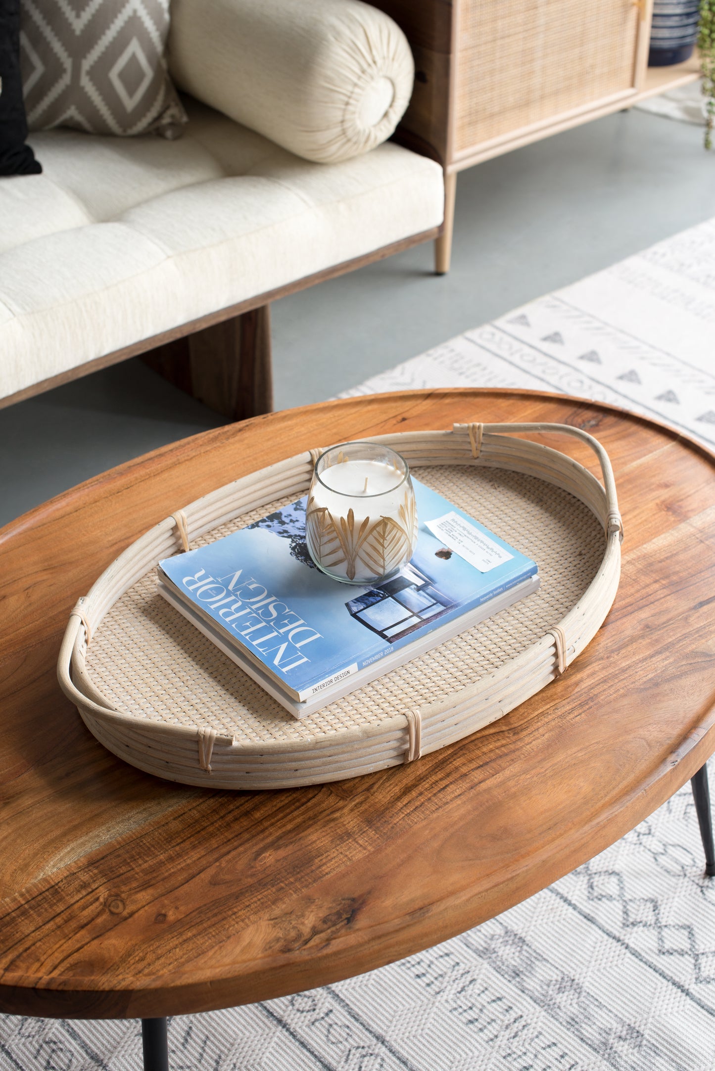 Oval woven rattan serving tray with a decorative candle and an interior design magazine