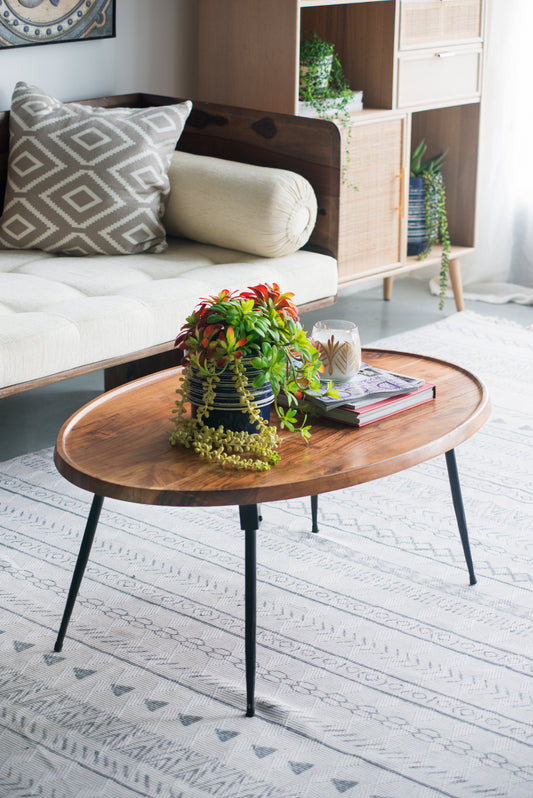 Oval wood coffee table with black metal legs and decorative plant