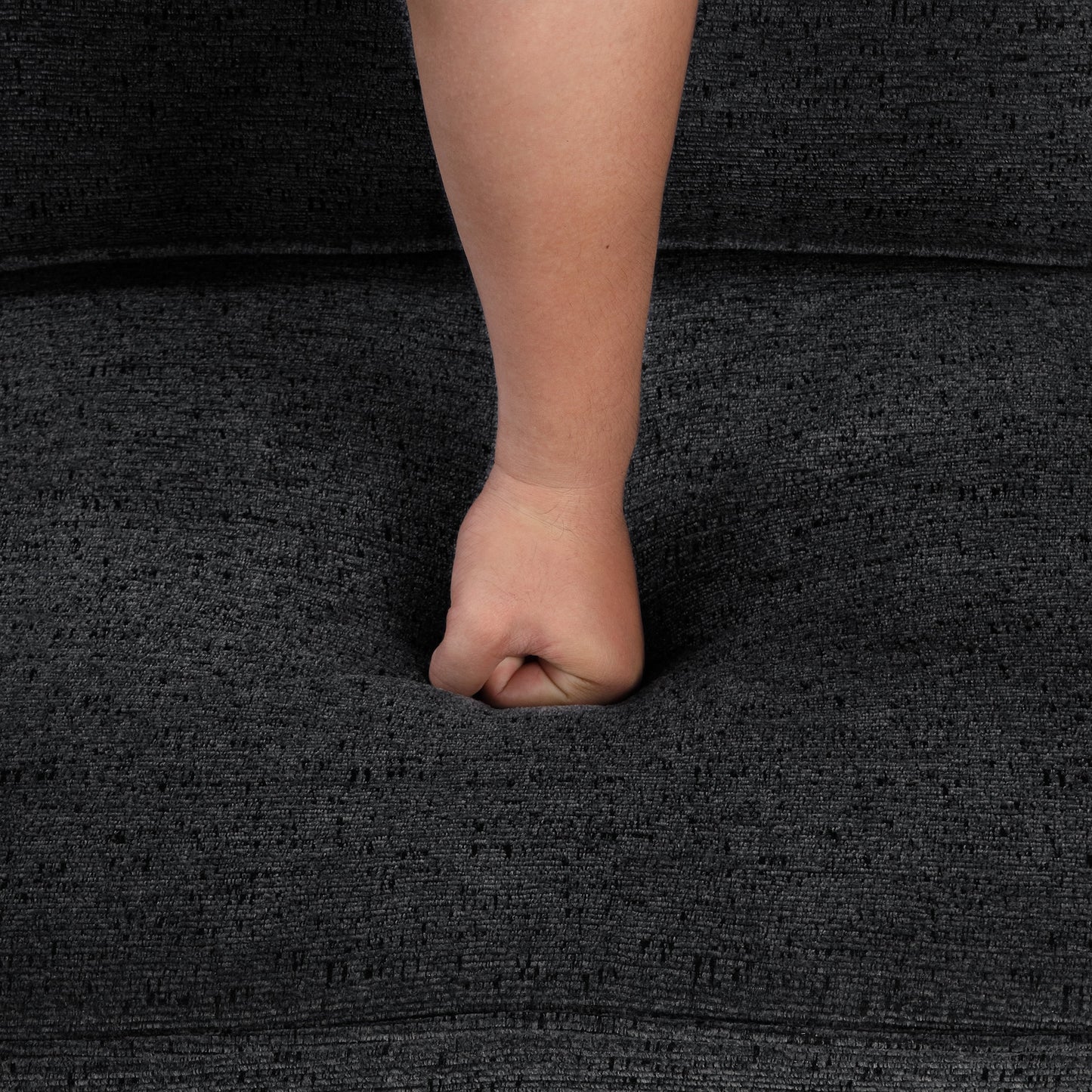 Dark gray textured fabric with a fist pressing into it showing plushness