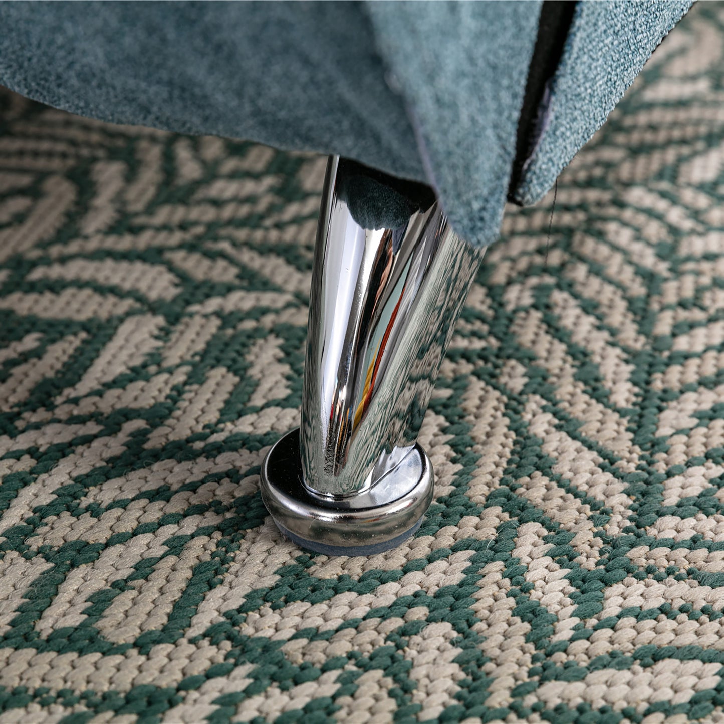Teal fabric sofa leg with chrome finish on geometric green and beige rug