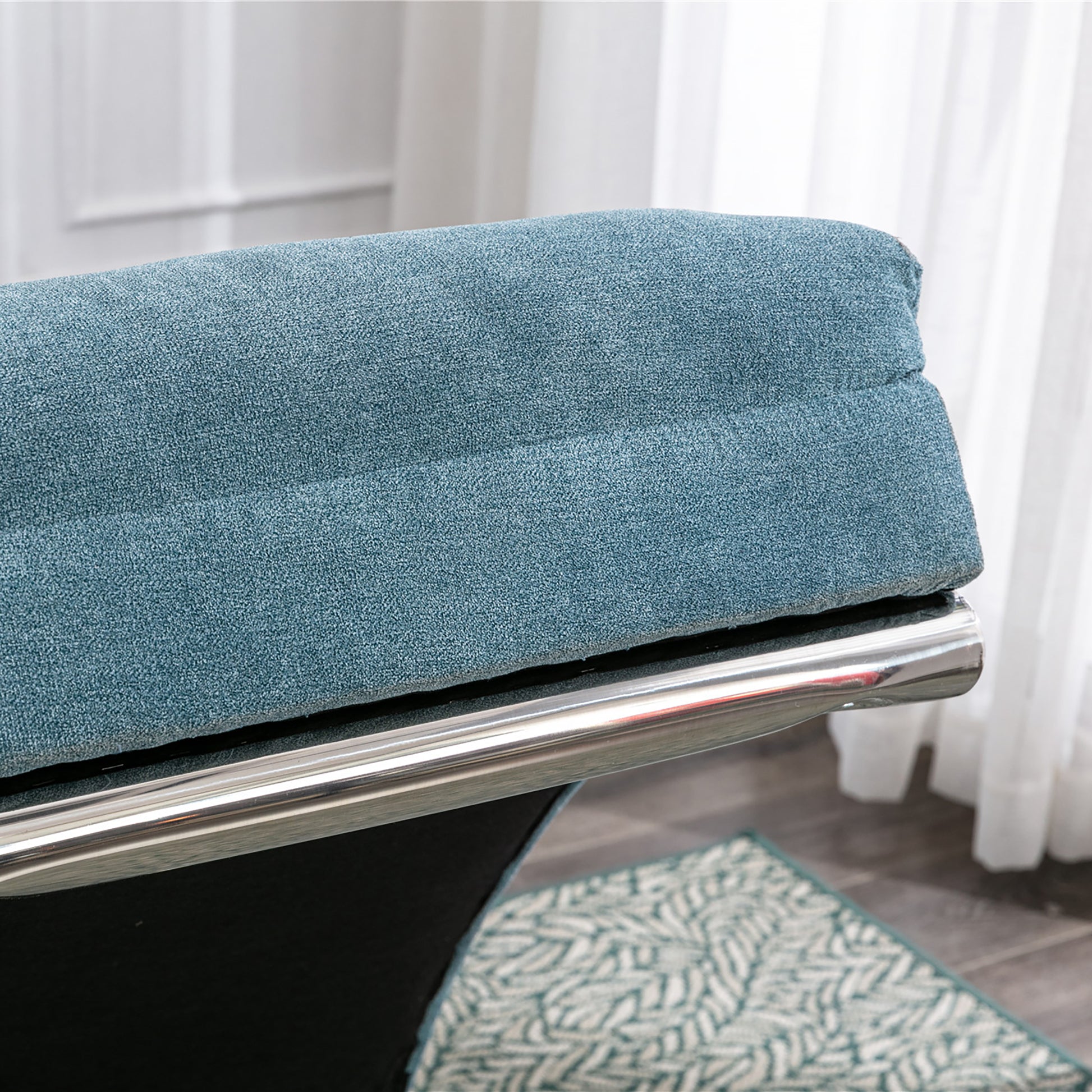 Closeup of a plush teal fabric armchair with a polished chrome accent frame
