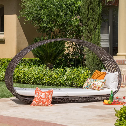 Oval rattan daybed with white cushions and decorative pillows for outdoor relaxation